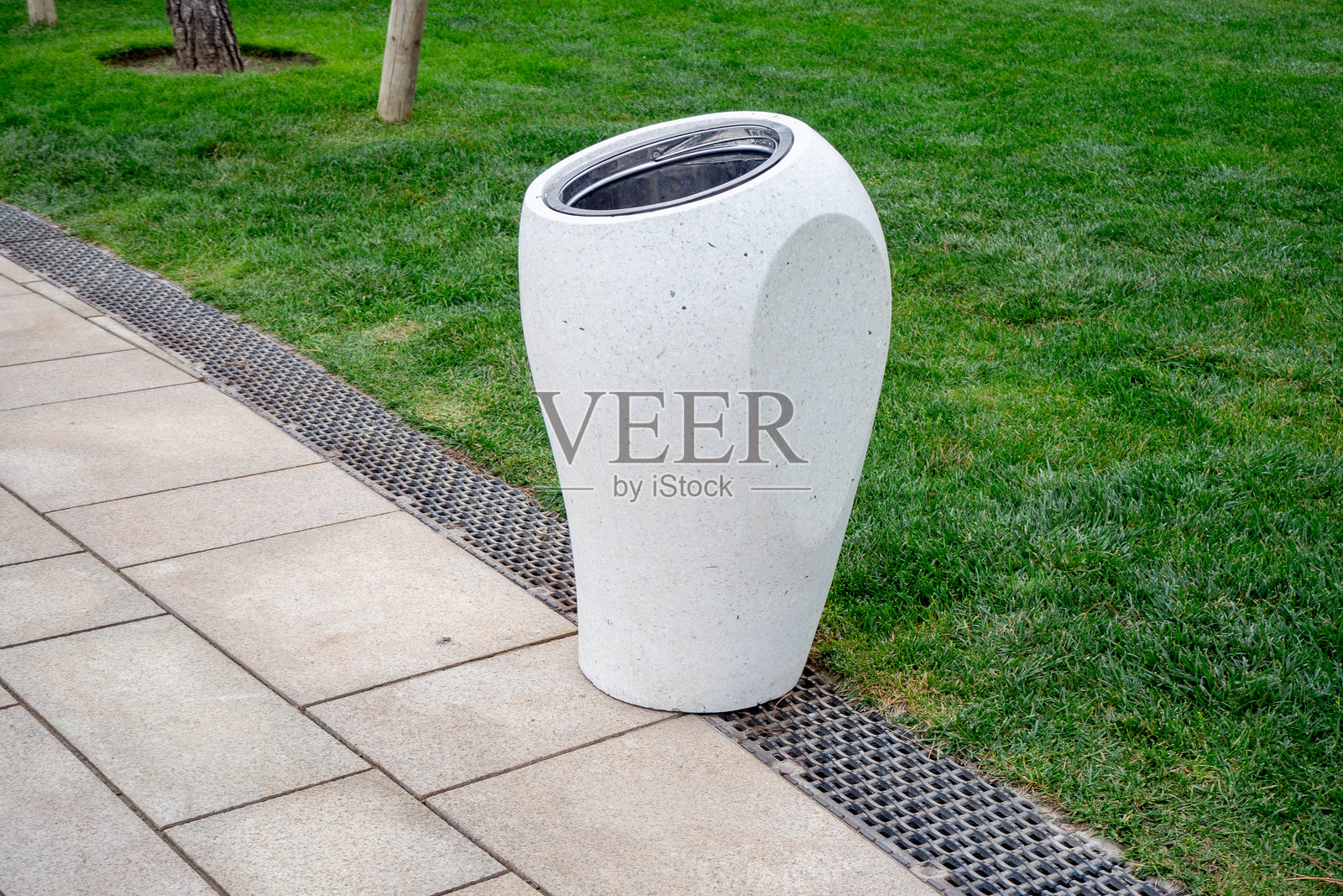 白色户外垃圾桶，设计现代，置于铺砌的人行道上，靠近绿草区。适用于街道家具、景观建筑、废物收集、城市环境。真实照片照片摄影图片