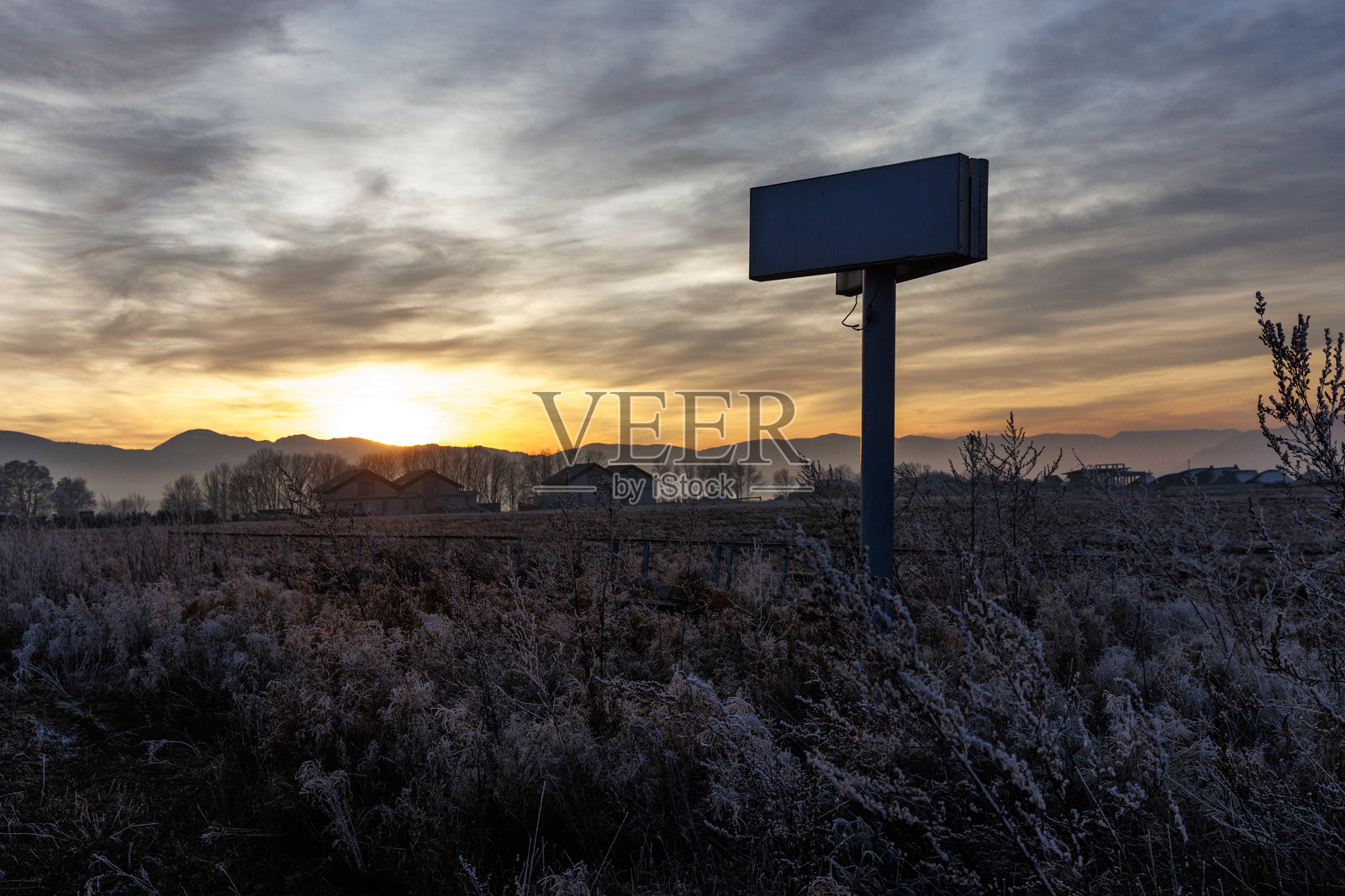 日出山峦映衬下的冰霜田野与空白广告牌照片摄影图片