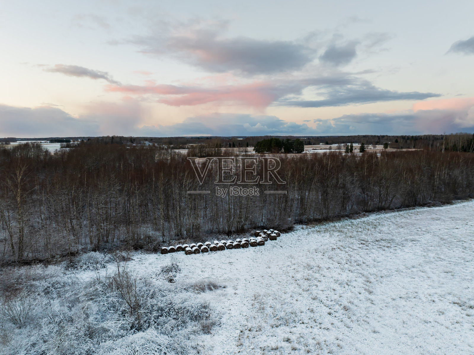 风景航拍无人机视角，爱沙尼亚冬季广袤的雪景，森林旁覆盖着干草包，在美丽的日落天空下。照片摄影图片