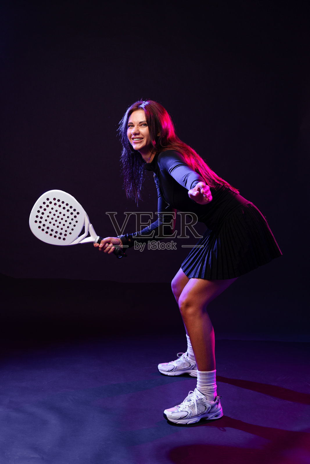 年轻女运动员在戏剧性的灯光下准备比赛，手中握着球拍照片摄影图片