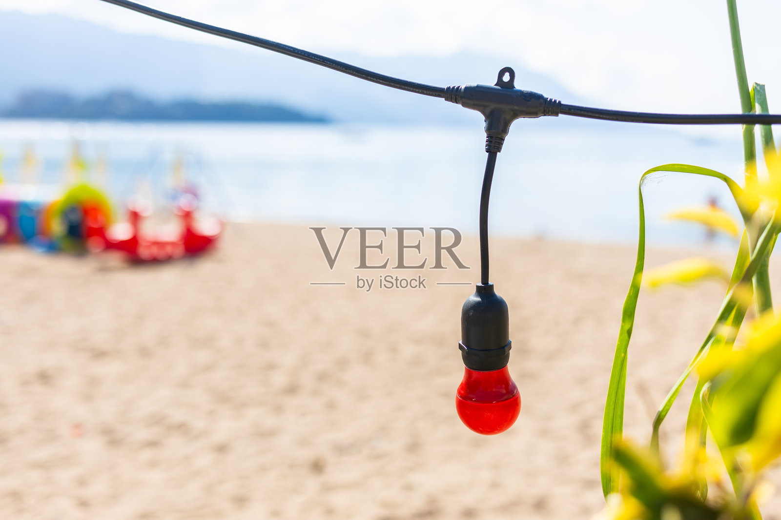 沙滩上的红色灯泡。装饰性照明元素，背景是模糊的海边。照片摄影图片