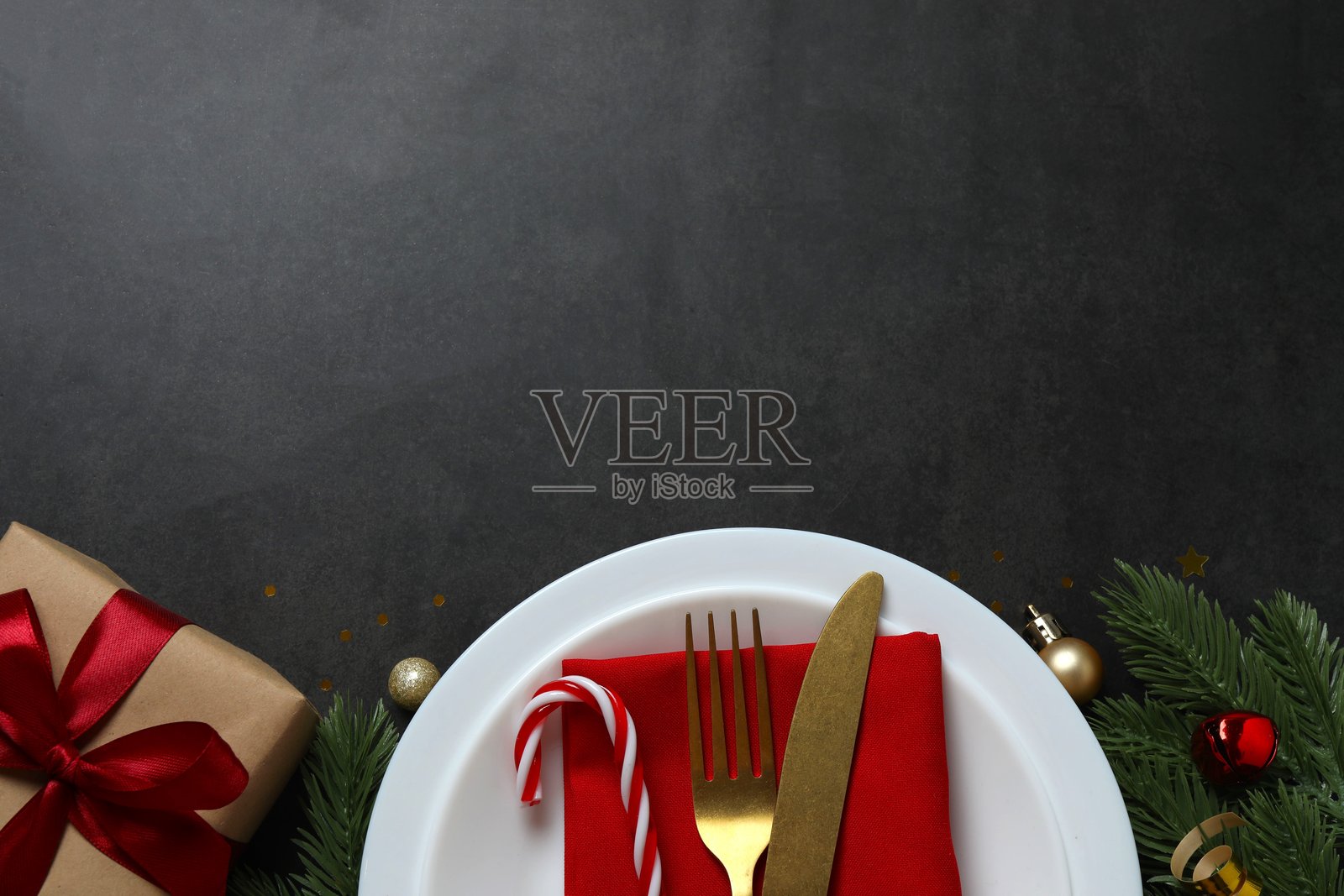 节日圣诞新年餐桌装饰，有松枝、红色装饰品和优雅的餐具，背景为深色。非常适合节日问候。照片摄影图片