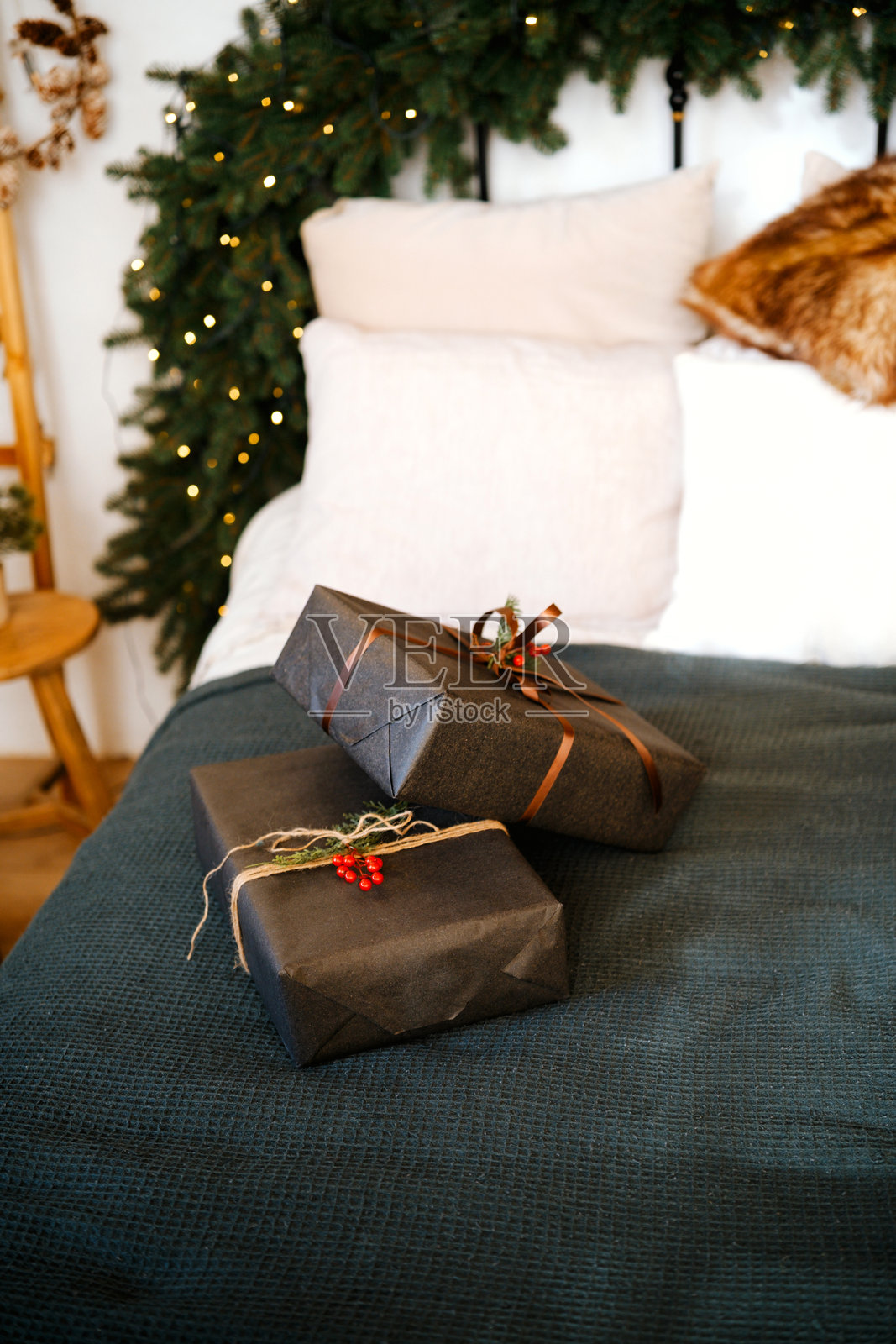 圣诞礼物用深色包装纸包裹，点缀着红浆果，放在床边，旁边是一棵闪烁着灯光的节日树。照片摄影图片