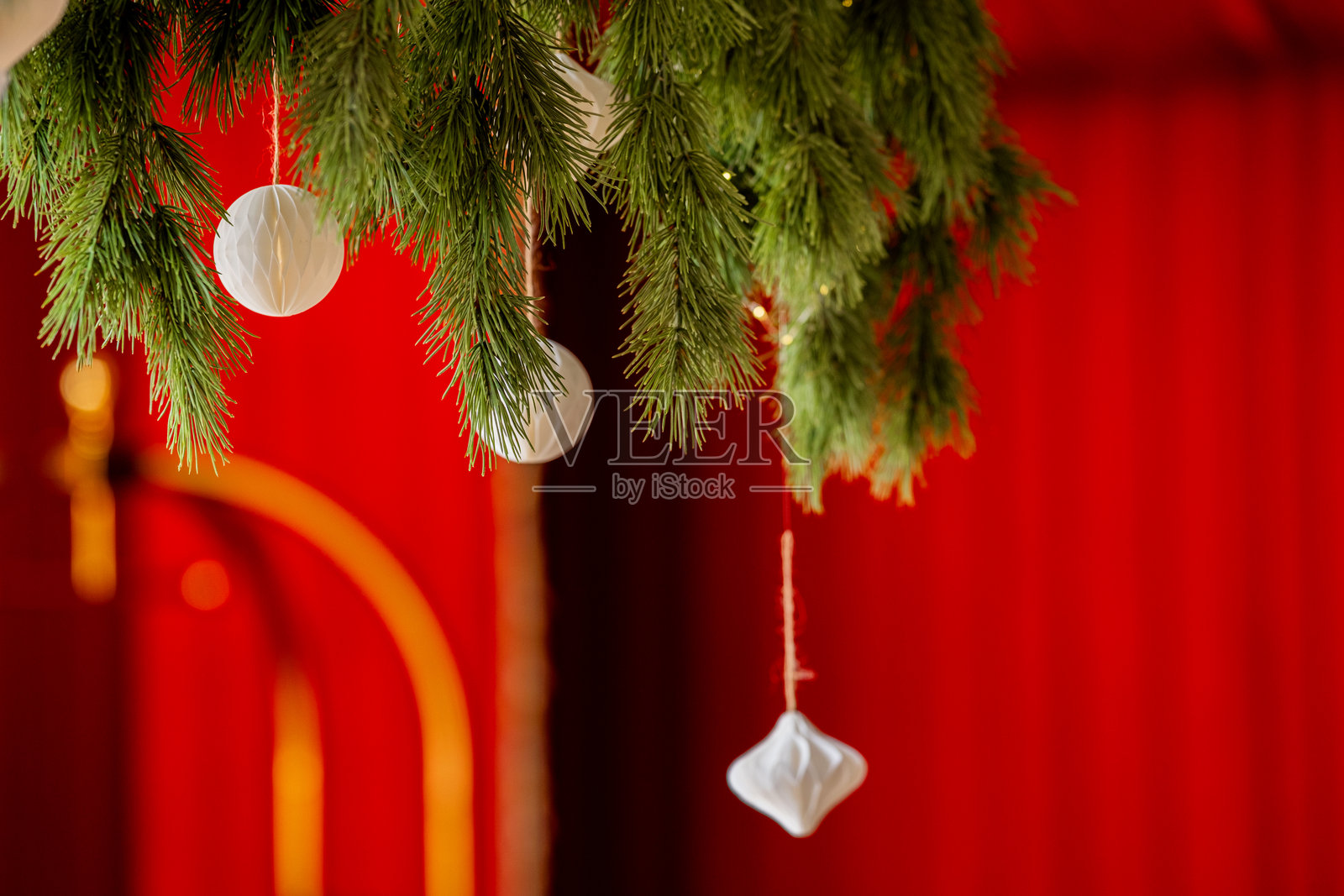 红背景上悬挂着带有白色纸质装饰的常绿树枝，节日装饰照片摄影图片
