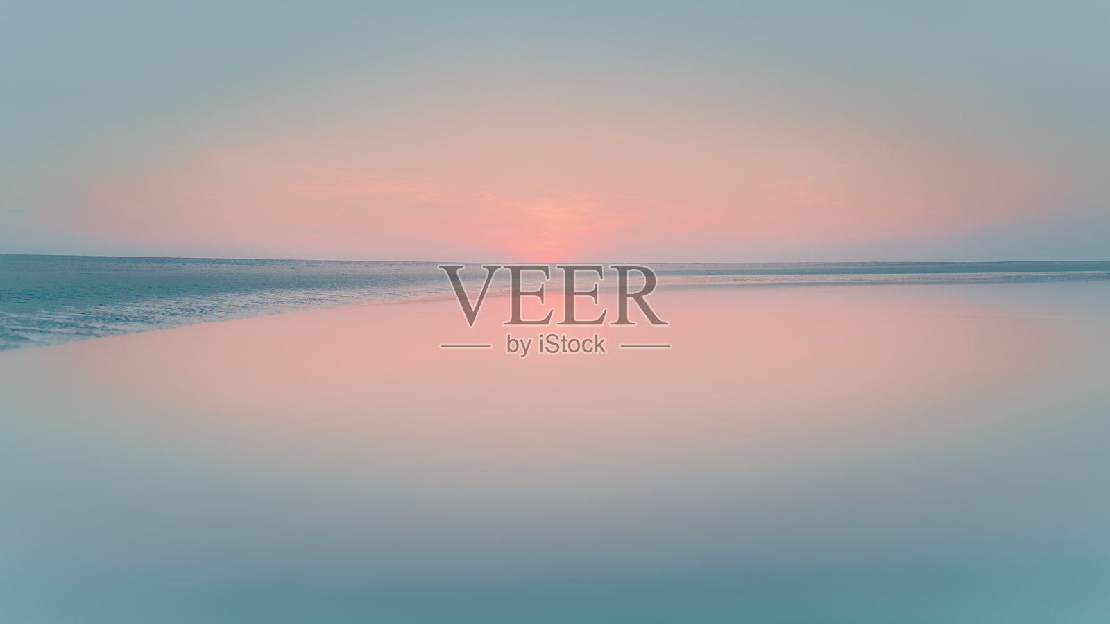 平静的水面映照着宽阔平坦的海滩上逐渐褪色的日落，地平线低垂。照片摄影图片