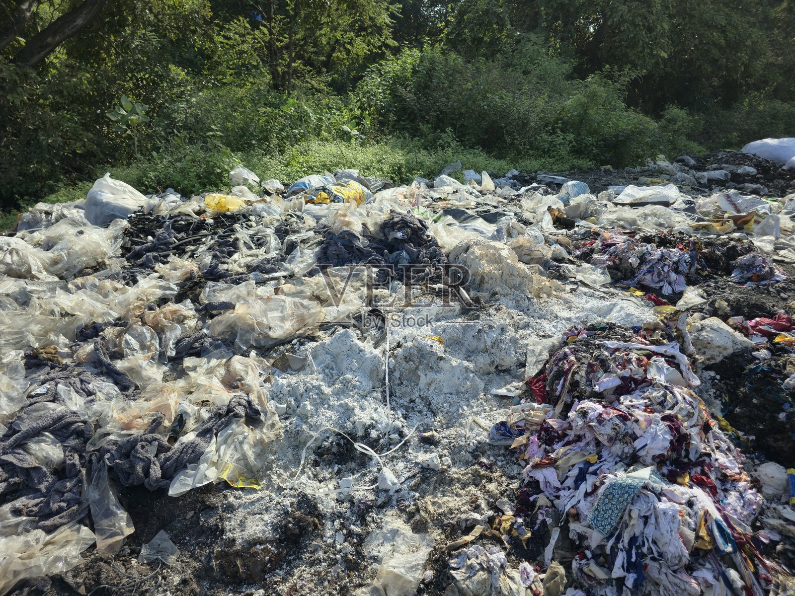 大堆混合垃圾和塑料废物倾倒在开阔地带，靠近绿色植被，显示出严重土地污染照片摄影图片