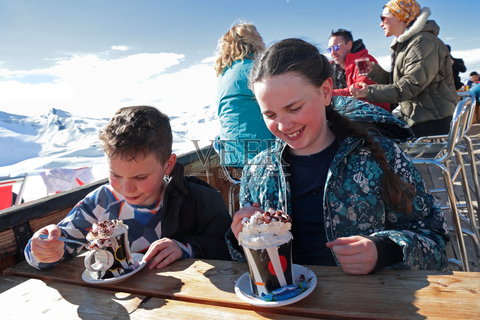 孩子们在滑雪度假村享用热巧克力，父母在远处照片摄影图片