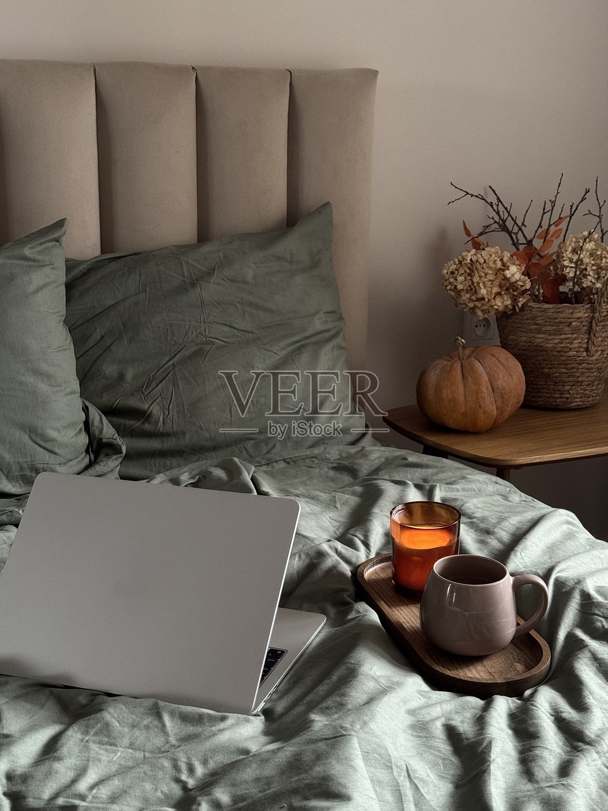 秋季家居装饰。舒适迷人的早餐与工作角落，燃烧的蜡烛，床上温馨早餐氛围的亲密宁静工作空间，配有笔记本。照片摄影图片