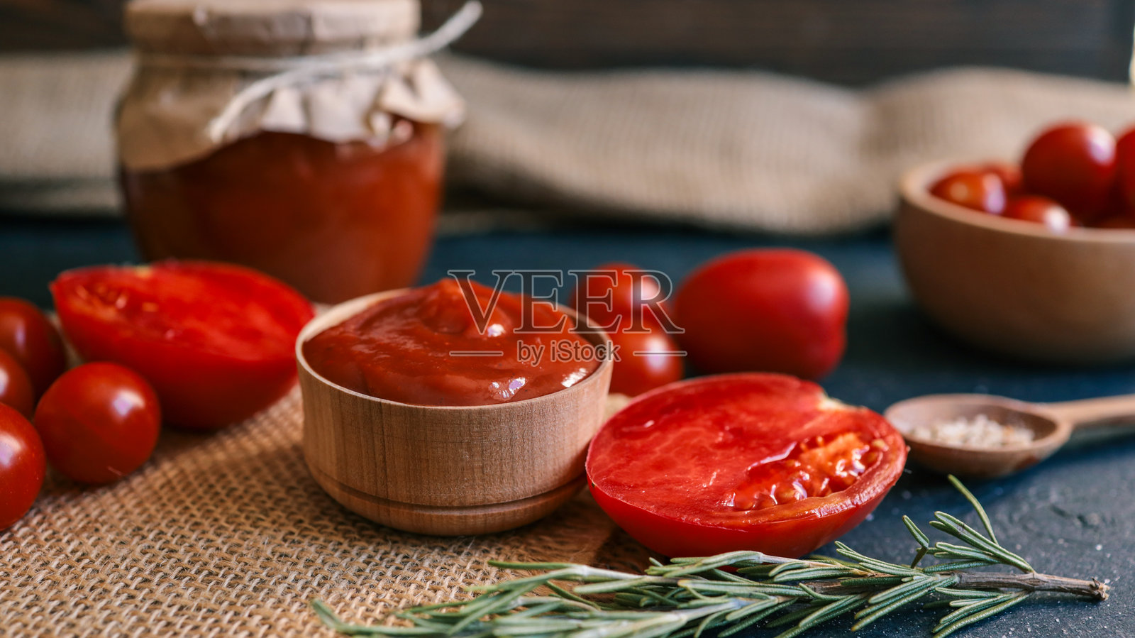 质朴的桌子上放着新鲜的番茄酱，配以番茄和迷迭香。照片摄影图片