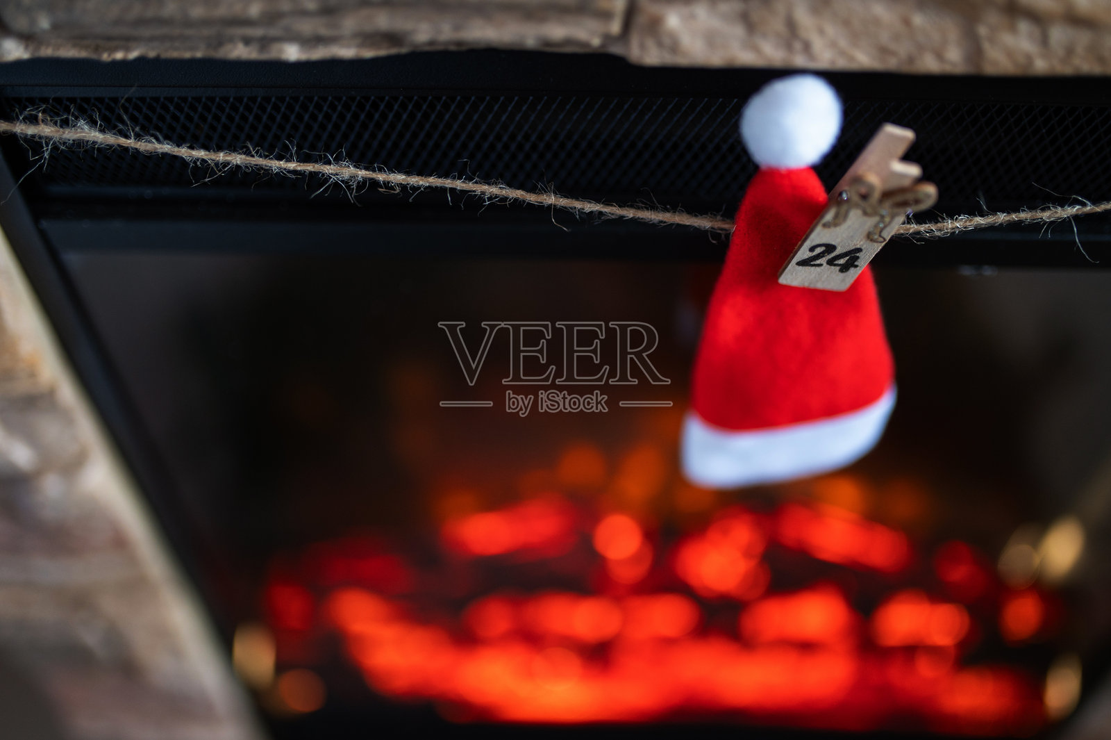 带有数字24的圣诞帽悬挂在舒适的圣诞壁炉上方的降临节花环上照片摄影图片