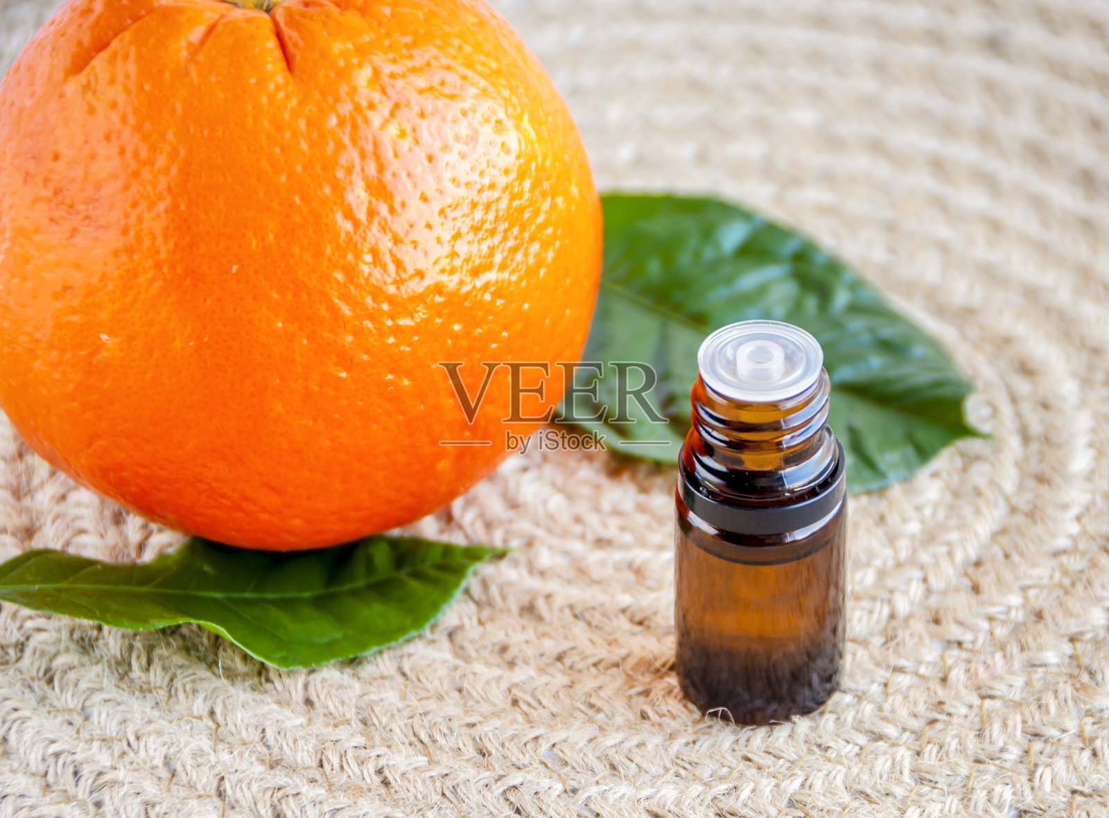 橙子精油。深色玻璃瓶装有橙子精油，橙子置于橙色背景上照片摄影图片