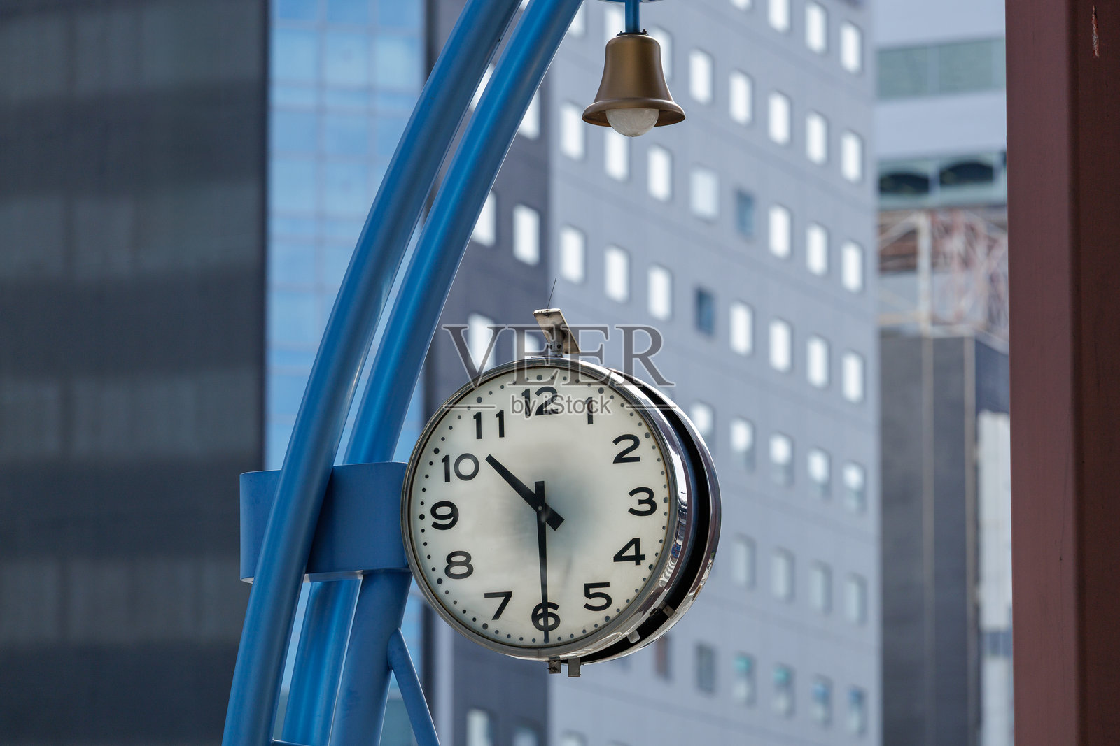 城市街道时钟悬挂在蓝色的金属框架上，背景是现代建筑照片摄影图片
