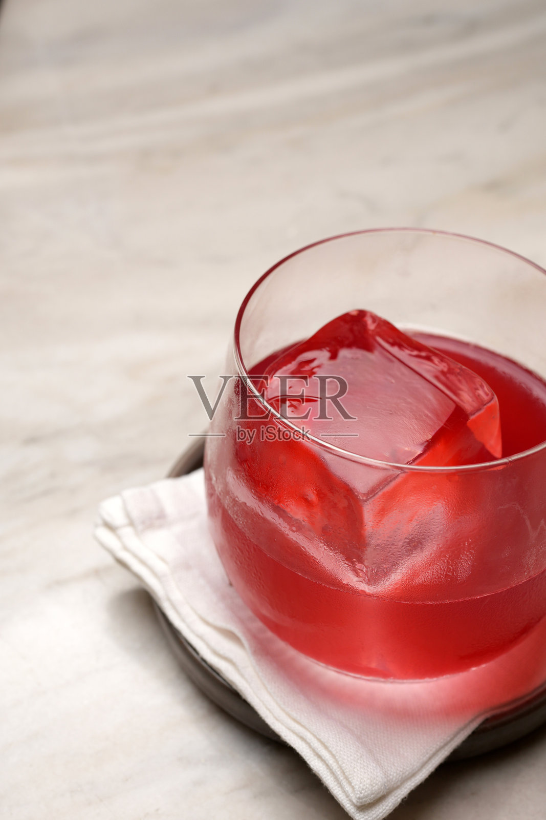 一个盛放在杯垫和餐巾纸上的鲜红色鸡尾酒，里面有一大块透明的冰块照片摄影图片
