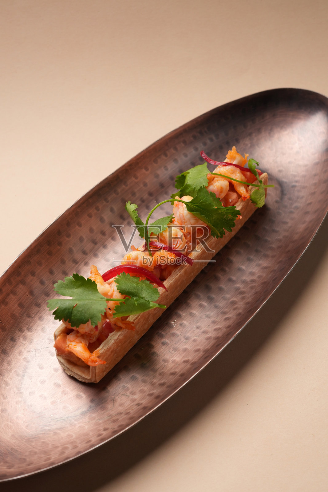 精致的开胃菜，特色是酥脆外壳中的虾仁和红洋葱，饰以香菜，盛放在狭窄的纹理铜盘上照片摄影图片