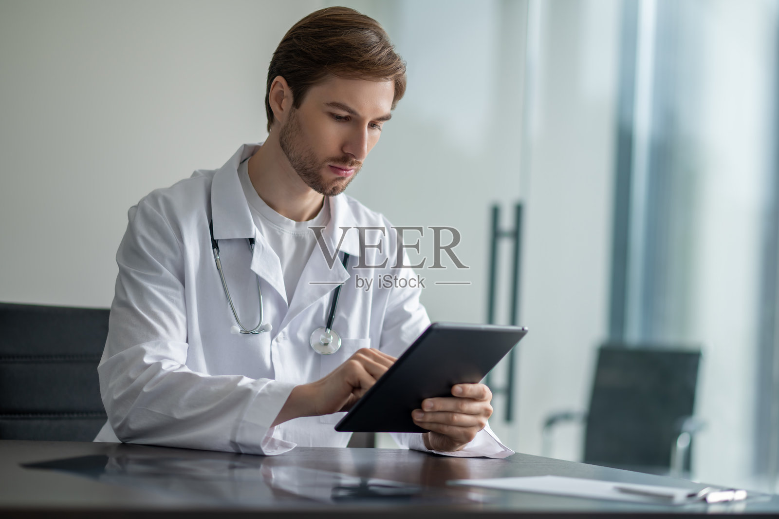 男医生坐在昏暗的办公桌前，在诊所里专注于黑色的平板电脑触摸屏照片摄影图片