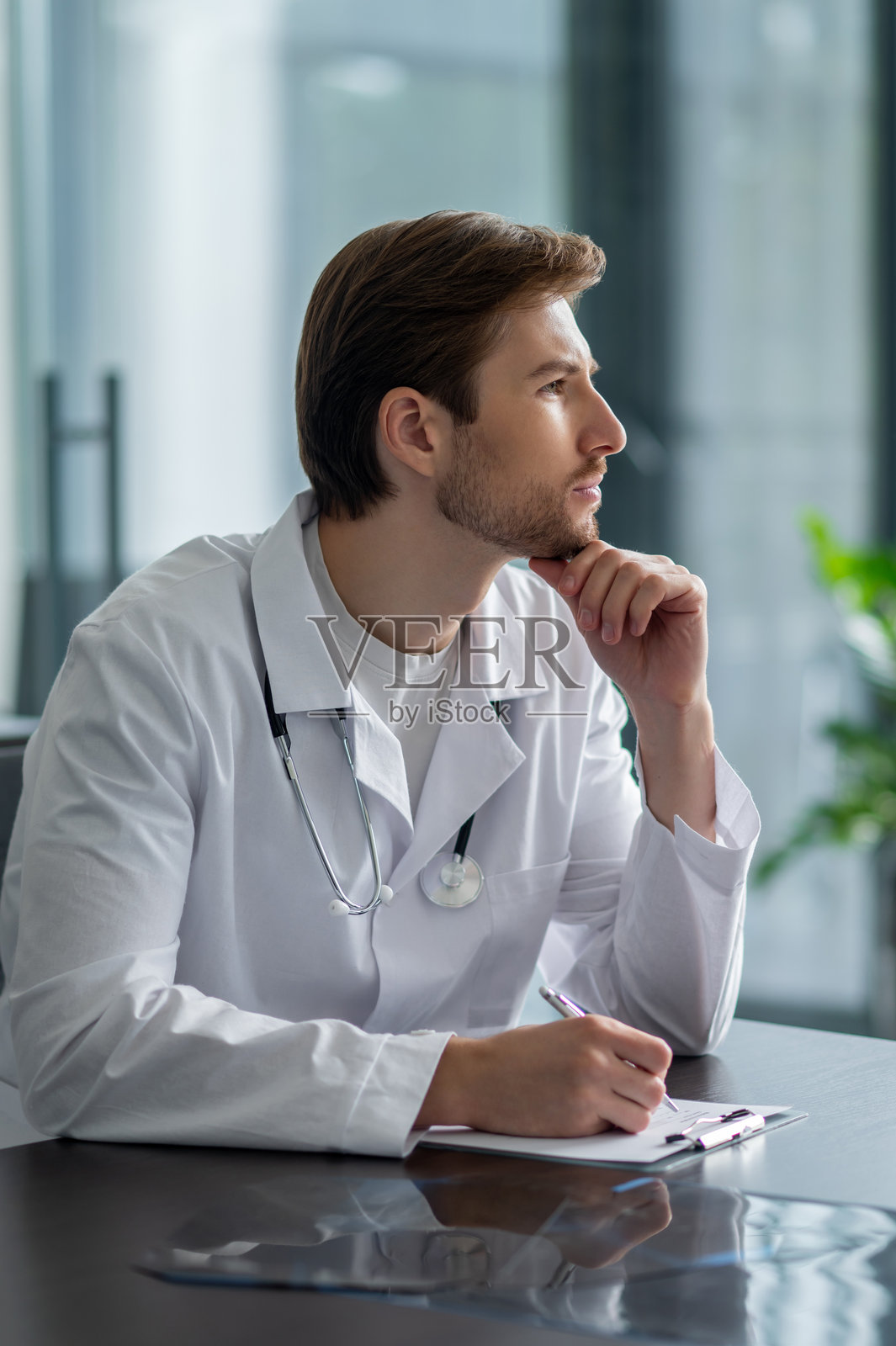 胡茬医生穿着白大褂在诊所的桌子旁用平板电脑书写照片摄影图片