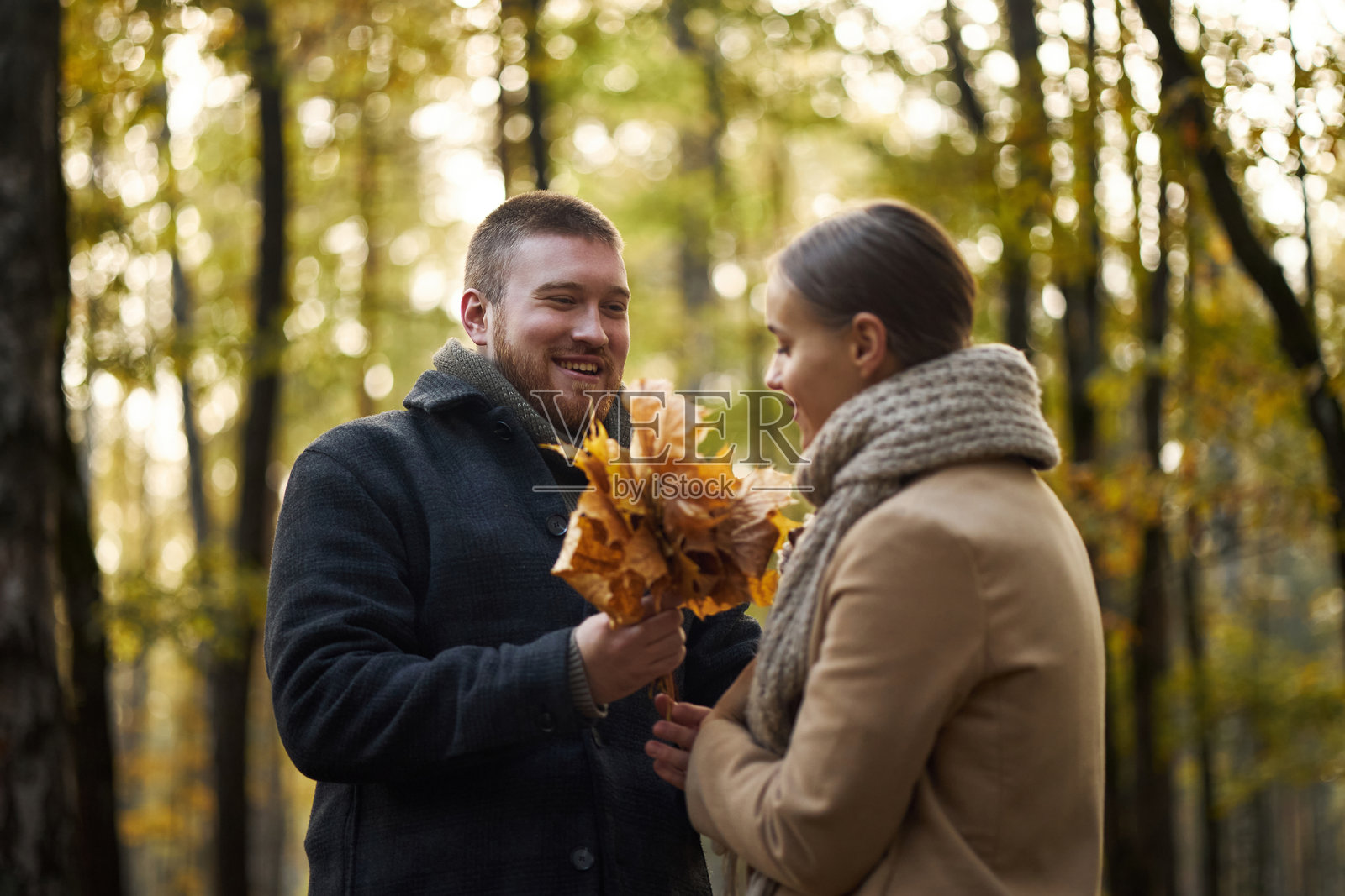 年轻男子在公园将秋叶花束送给年轻女子照片摄影图片