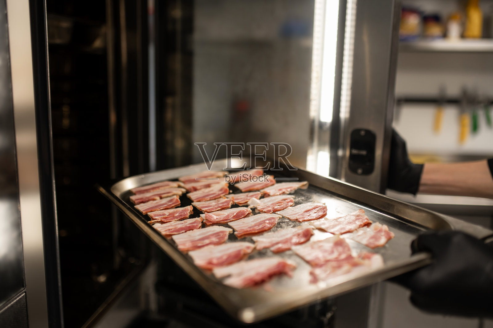 厨师的手在烤箱附近拿着装有生培根的托盘照片摄影图片