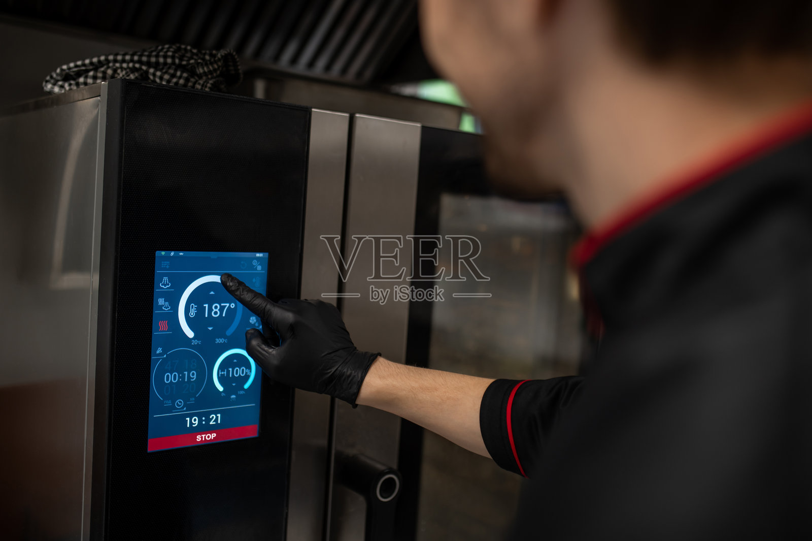 身穿黑色制服的男士正在智能厨房电器上设置加热功能照片摄影图片