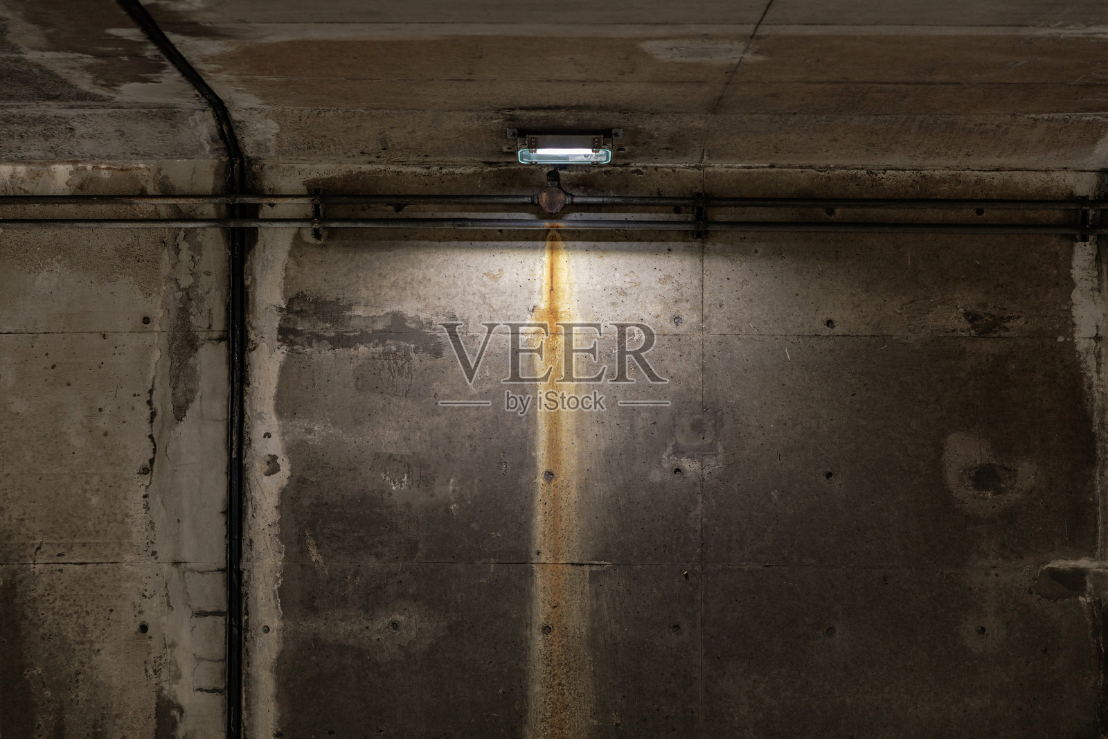 昏暗地下通道里的锈迹斑斑的混凝土墙和顶灯照片摄影图片