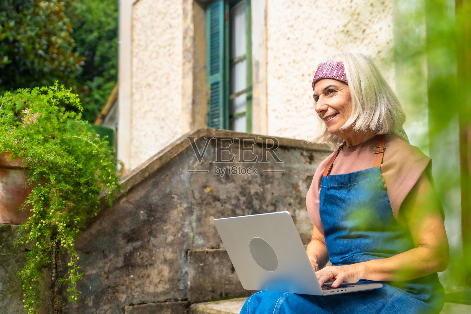 年长女性微笑着在户外使用笔记本电脑远程工作照片摄影图片