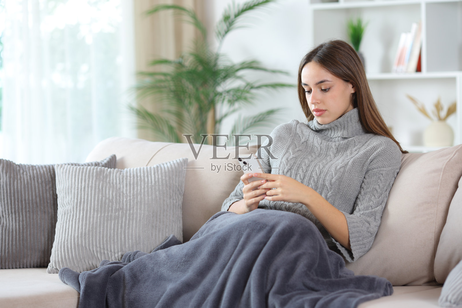 身穿灰色衣服的女子在冬天于沙发上使用手机照片摄影图片