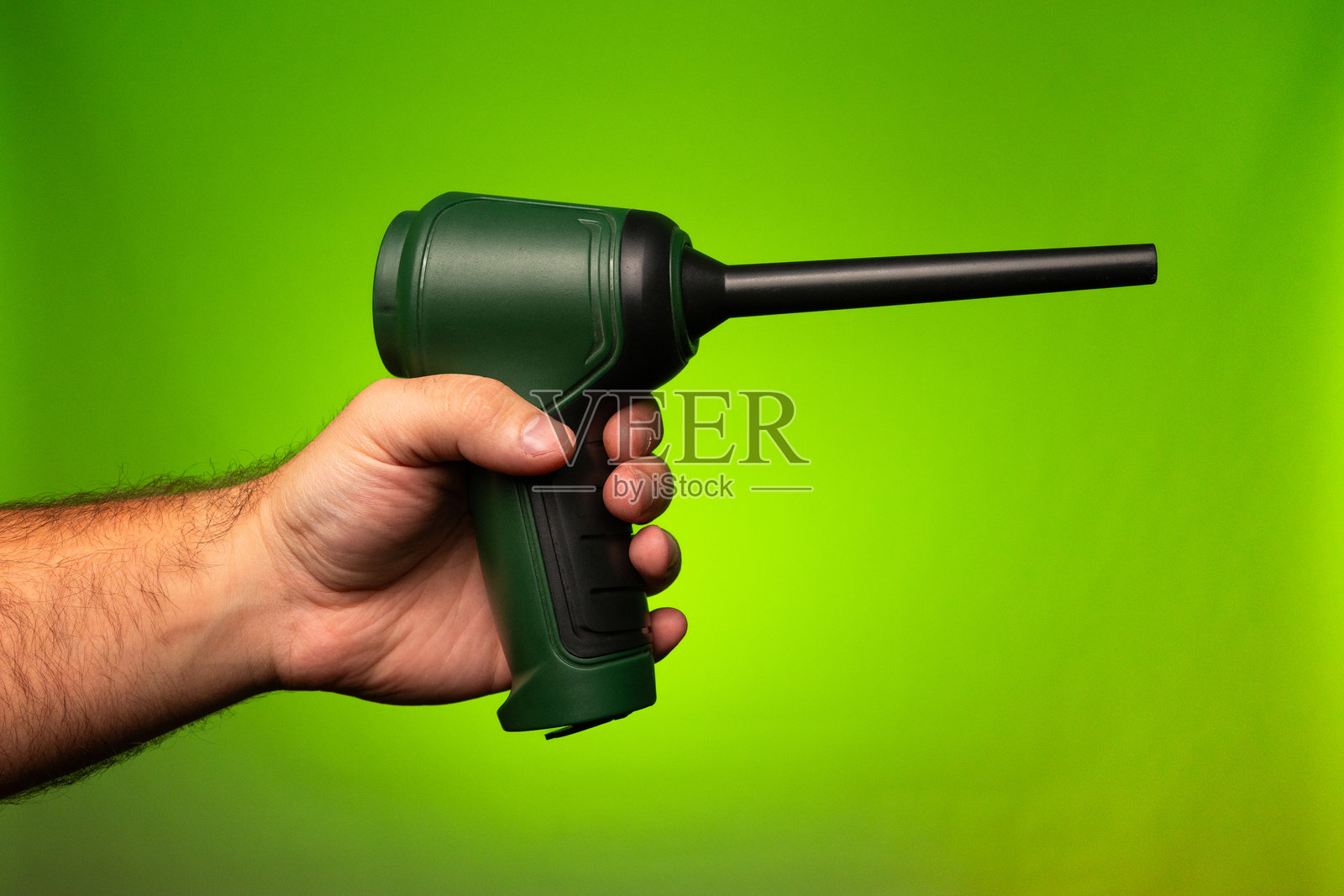 一名男子手持小型电池供电的绿色吸尘器。一名男子手持小型空气压缩机。一名男子手持小型吹风机。小型吸尘器。小型吹风机。小型空气压缩机。照片摄影图片