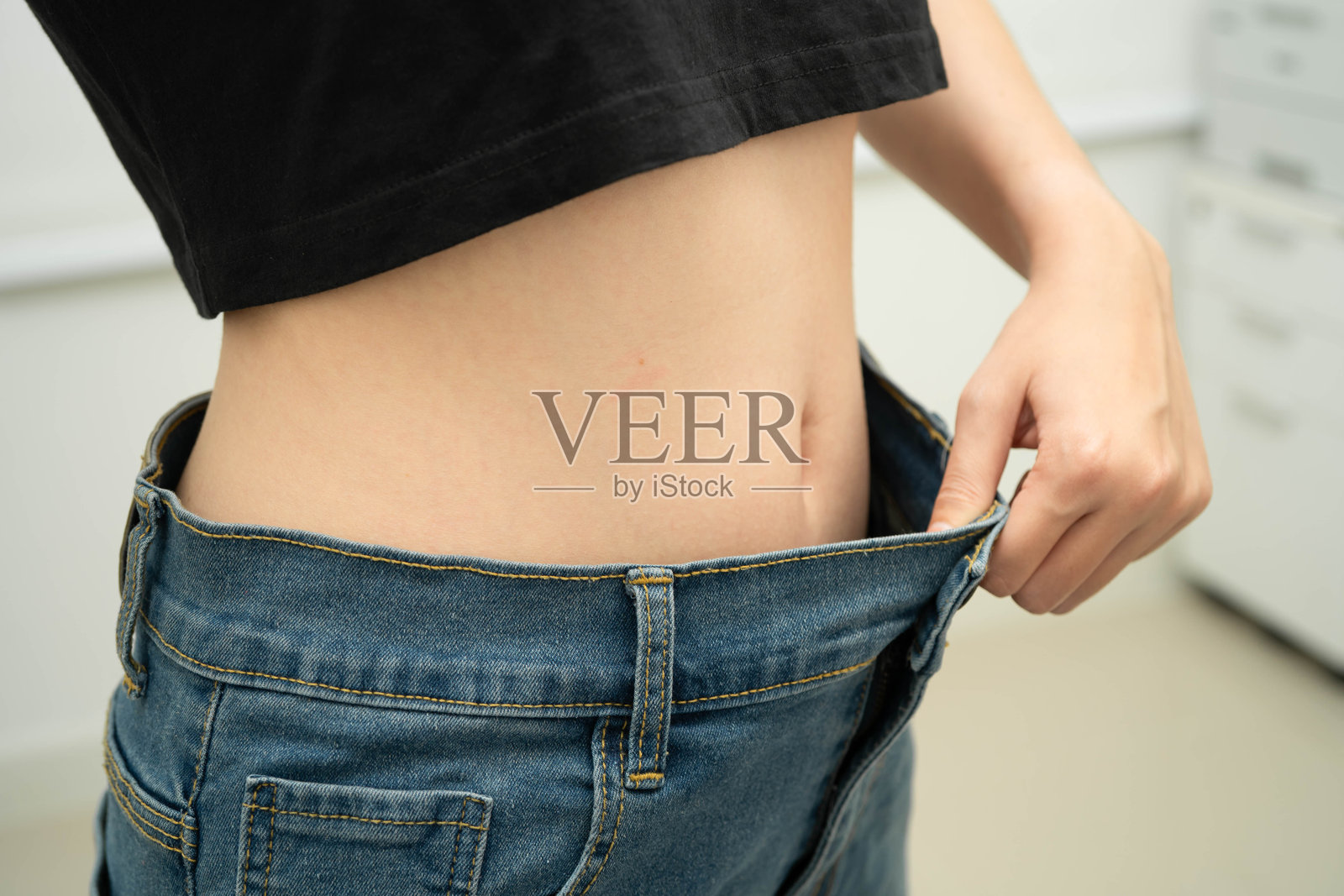 一位年轻的亚洲女性穿着宽松的裤子和超大号牛仔裤，正在减肥。照片摄影图片