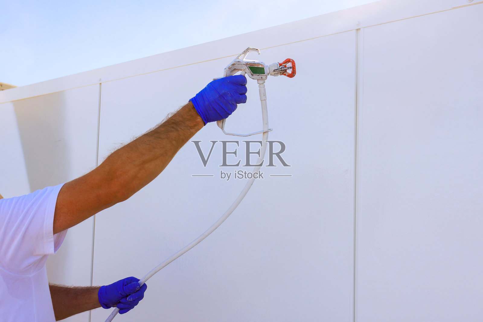 一个人正在阳光明媚的户外环境中，使用喷漆枪在墙上喷涂新漆照片摄影图片