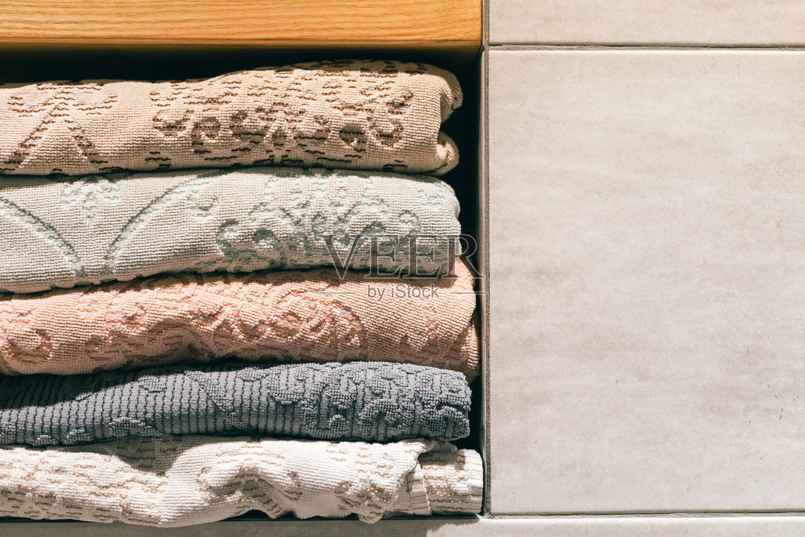 浴室架子上叠放着带有花纹的折叠毛巾，背景是瓷砖墙和木质元素。照片摄影图片