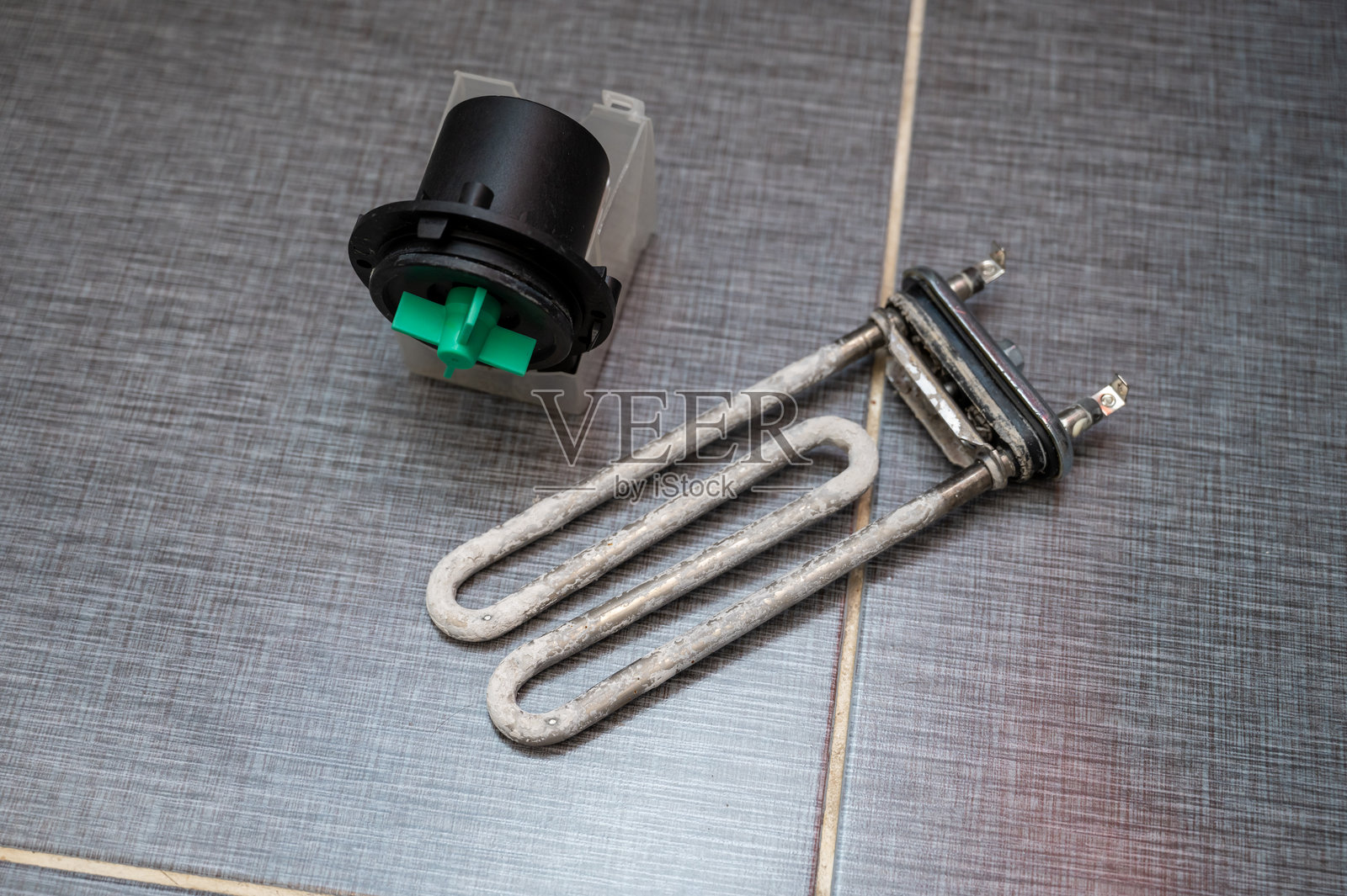 拆卸后放置在瓷砖地板上的洗衣机加热元件和水泵电机照片摄影图片