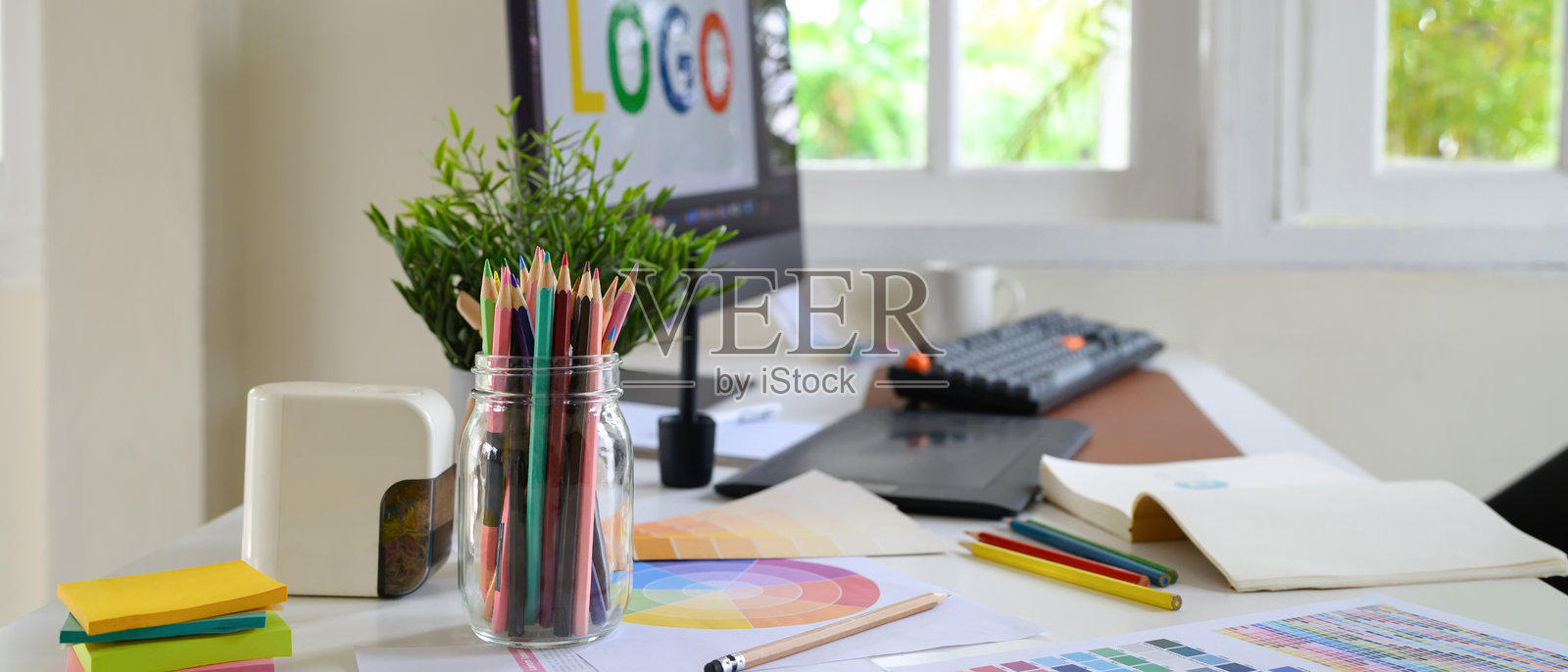 创意设计工作空间，配有罐子里的彩色铅笔、色板和显示着标志设计的电脑屏幕。照片摄影图片