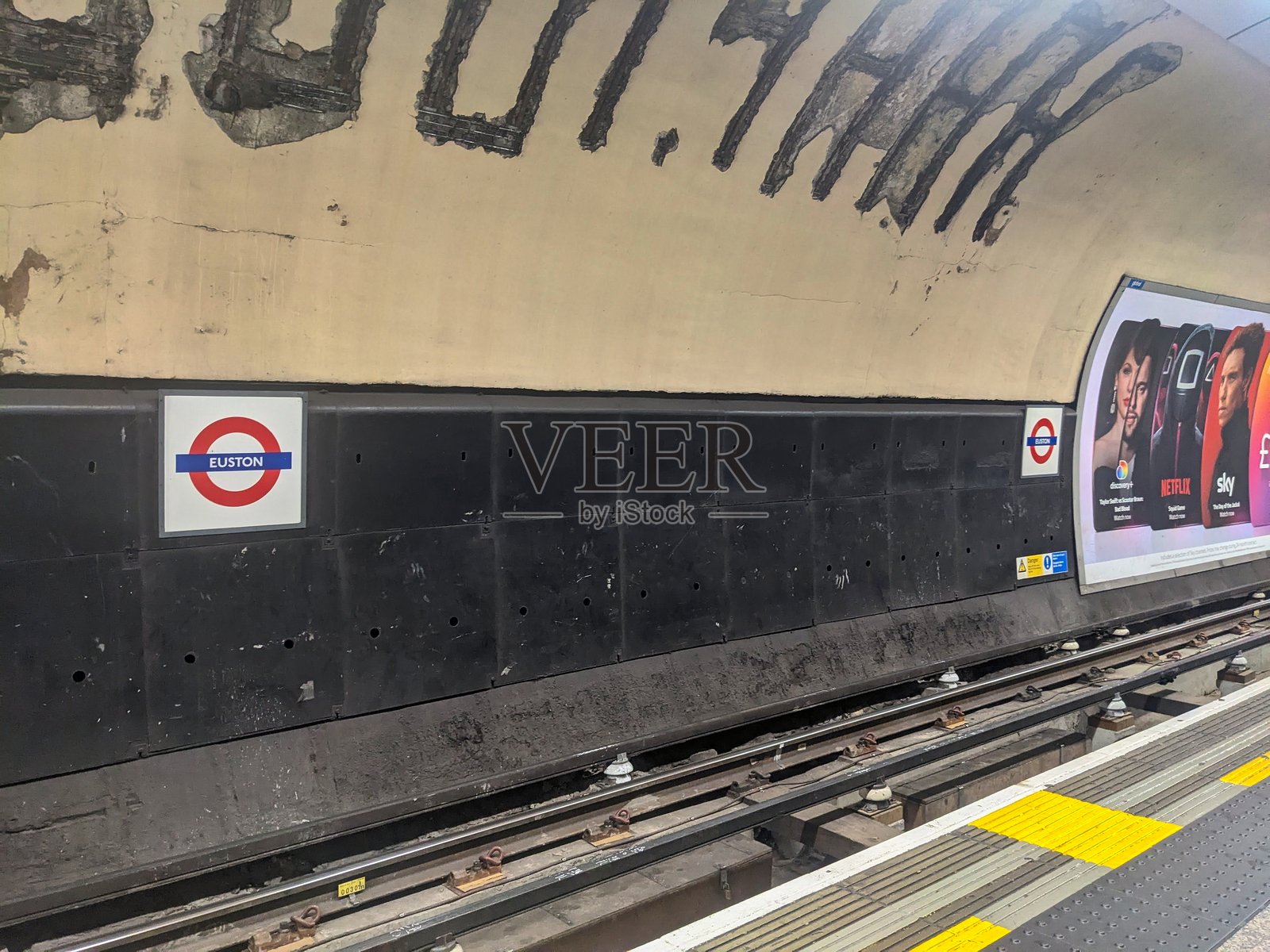 标志性的尤斯顿车站圆形标志和伦敦地铁轨道旁陈旧的隧道壁照片摄影图片