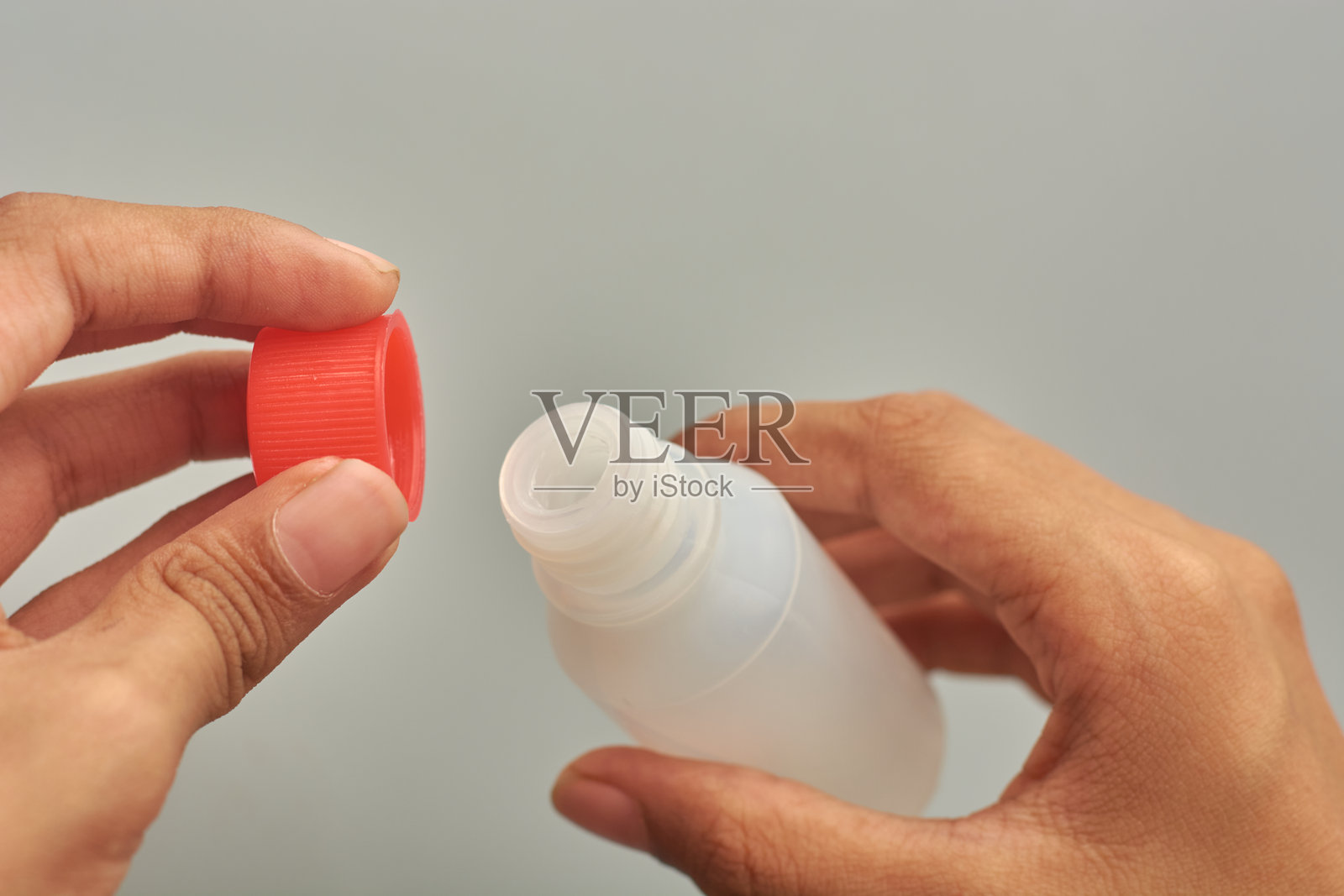 一只手打开带有红色盖子的塑料瓶，孤立的照片摄影图片