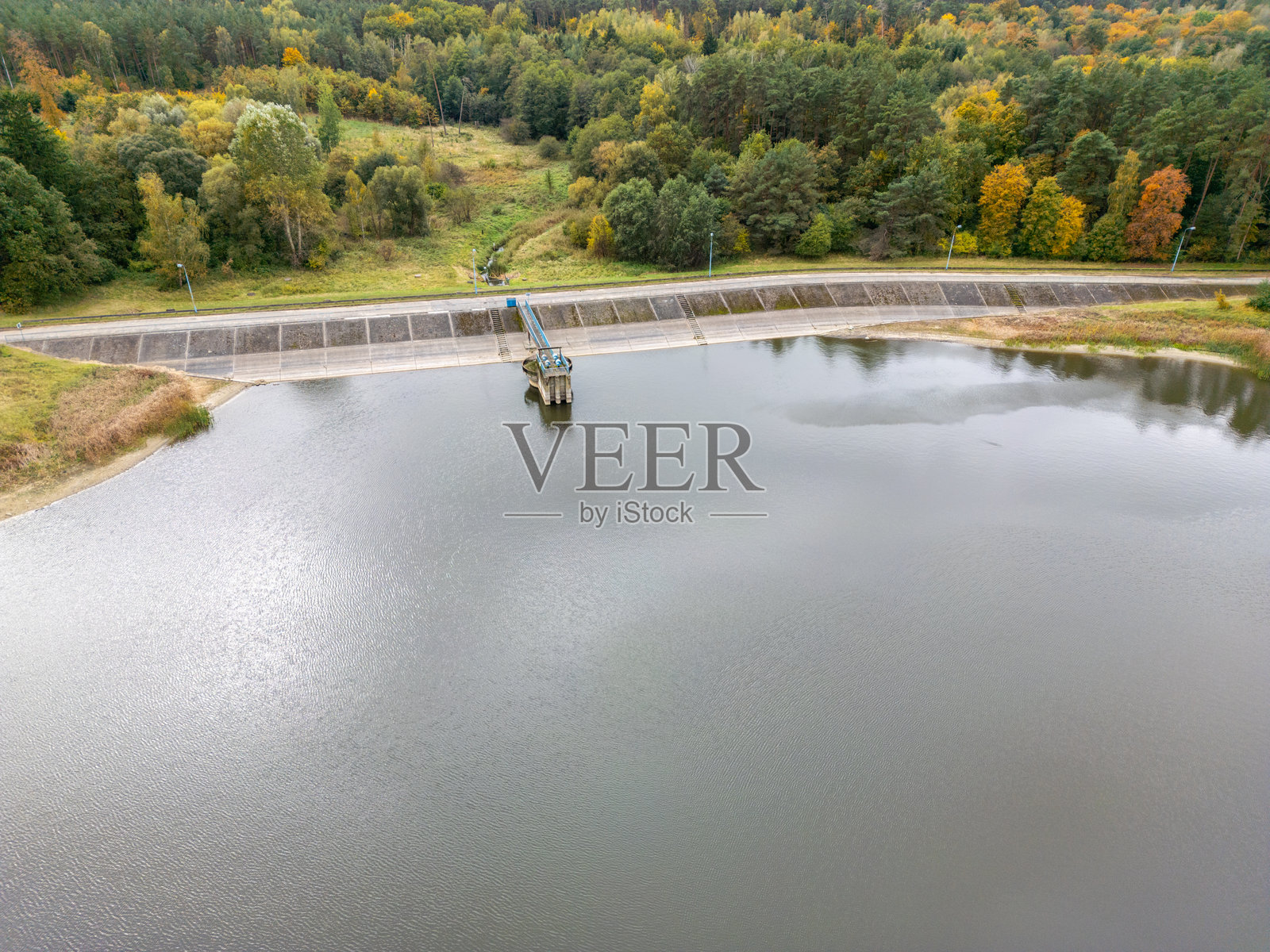空中俯瞰水库大坝，展示了郁郁葱葱的秋季森林景观中的水利基础设施。照片摄影图片