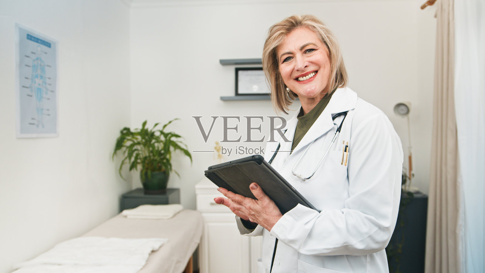 微笑的女医生穿着白大褂，手持平板电脑在诊所为患者提供护理照片摄影图片