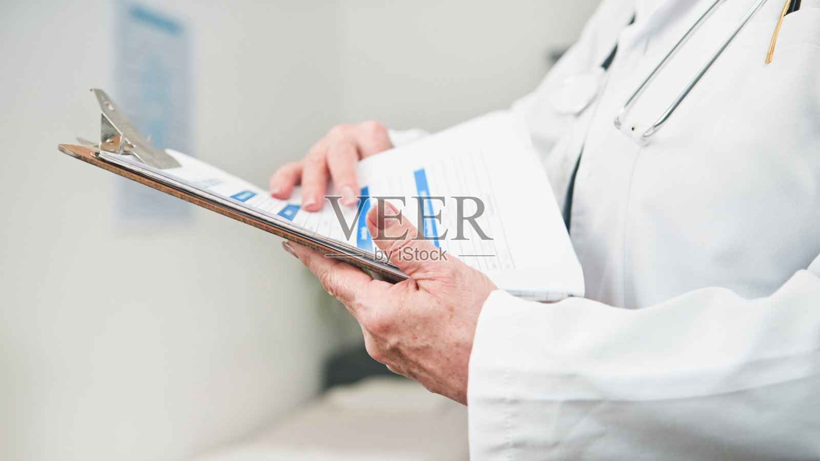 医生在医院的诊疗环境中，手持夹板上的病历，并佩戴着听诊器进行查阅。照片摄影图片