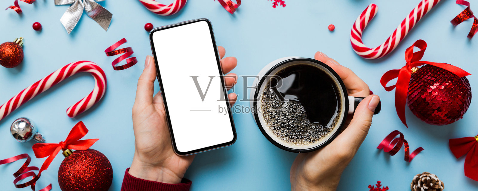 俯视女性手持智能手机和热咖啡杯。彩色背景上的圣诞装饰。照片摄影图片