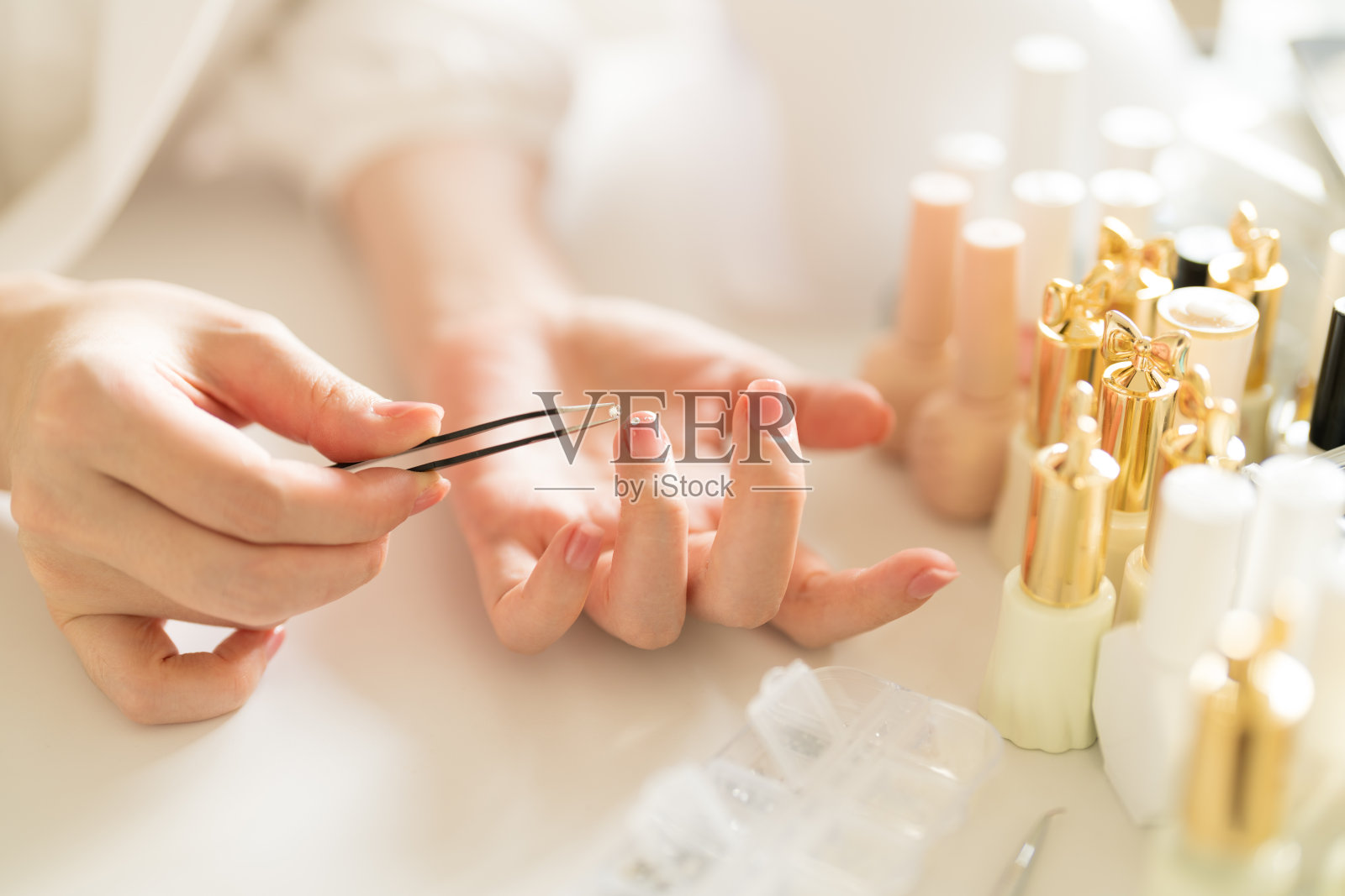 用钳子夹住一颗钻石，将其贴在指甲上。照片摄影图片