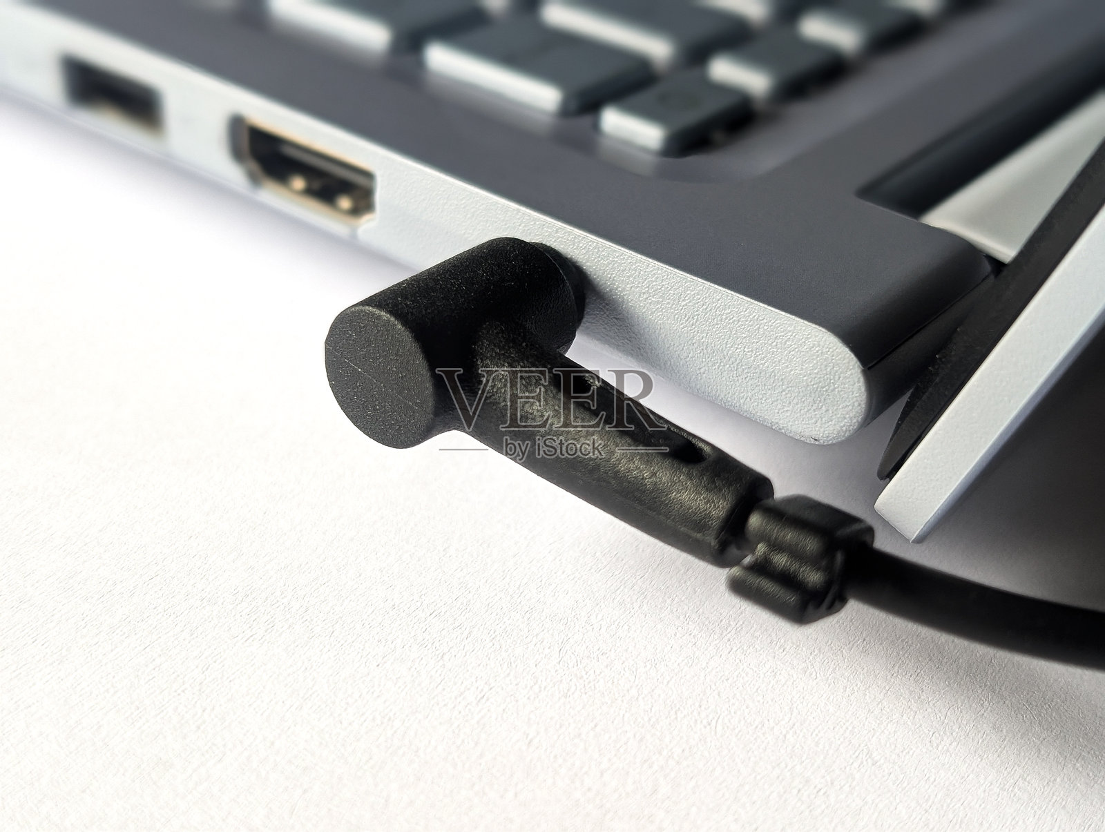 特写：黑色电源插头连接到银色笔记本电脑的侧面端口，可见 HDMI 和 USB 端口照片摄影图片