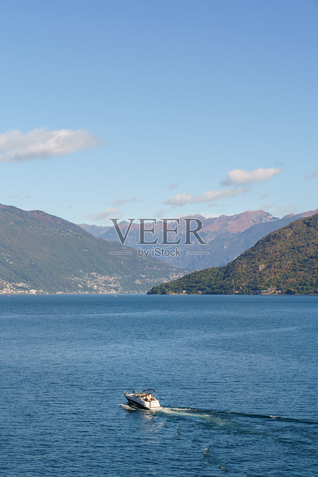 意大利马焦雷湖，背景为绿色山峦，天气晴朗，阳光明媚，水面平静，一艘小型摩托艇在水面上行驶。照片摄影图片