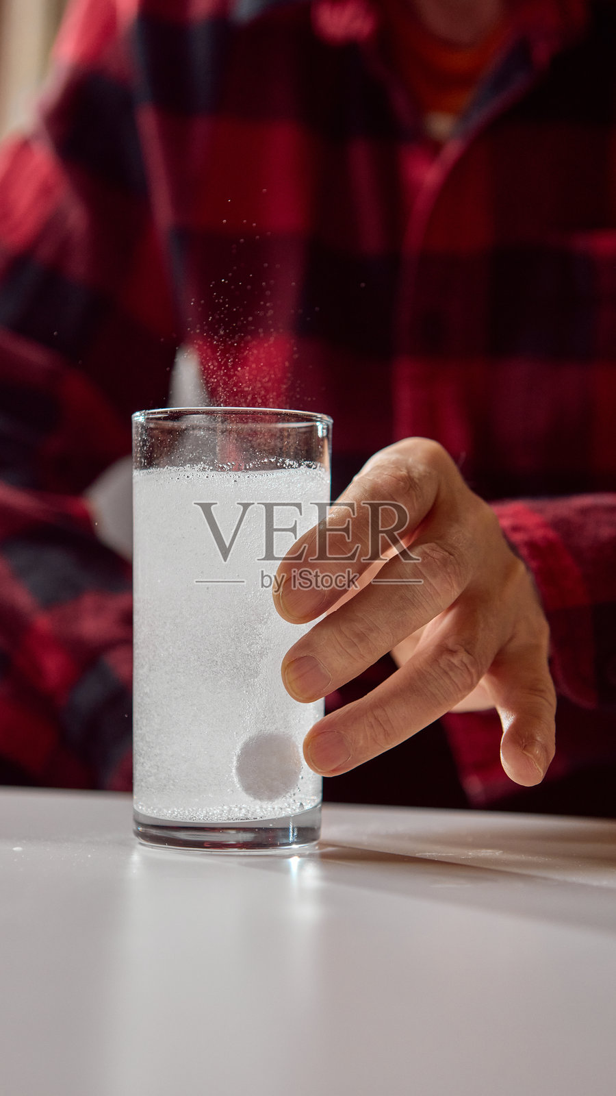 老人手触碰玻璃杯，杯中有溶解的泡腾片照片摄影图片