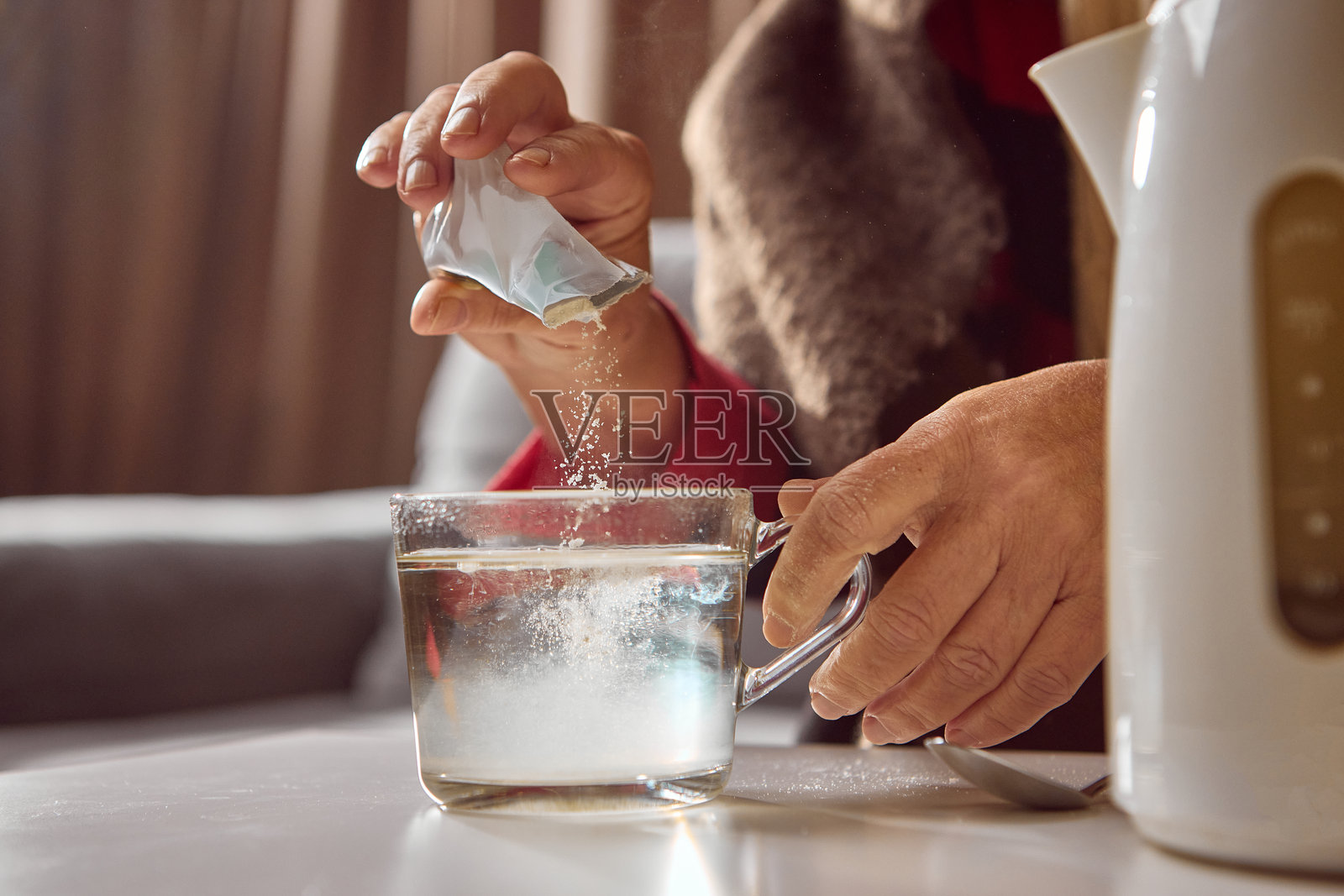 一位老年女性正在用热水在玻璃杯中溶解冲剂照片摄影图片