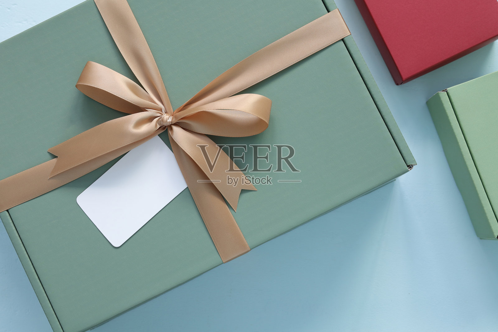 优雅的鼠尾草绿礼品盒，饰有金色丝带蝴蝶结和空白白色标签，孤立在蓝色背景上。俯视平面图，展示用于圣诞节、生日、纪念日或节日庆祝活动的礼物。照片摄影图片