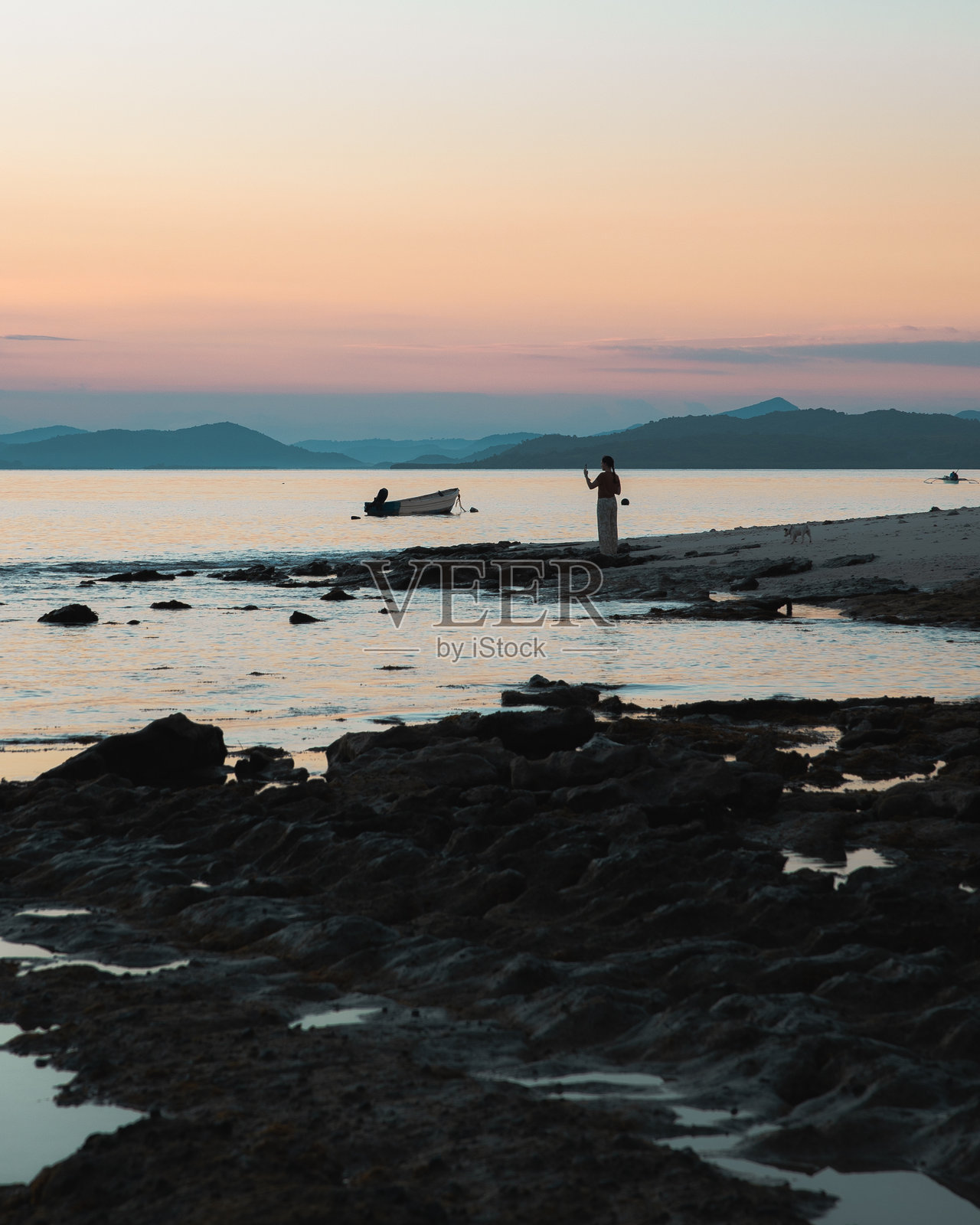 日落时分，女子剪影在岩石海滩上拍照照片摄影图片