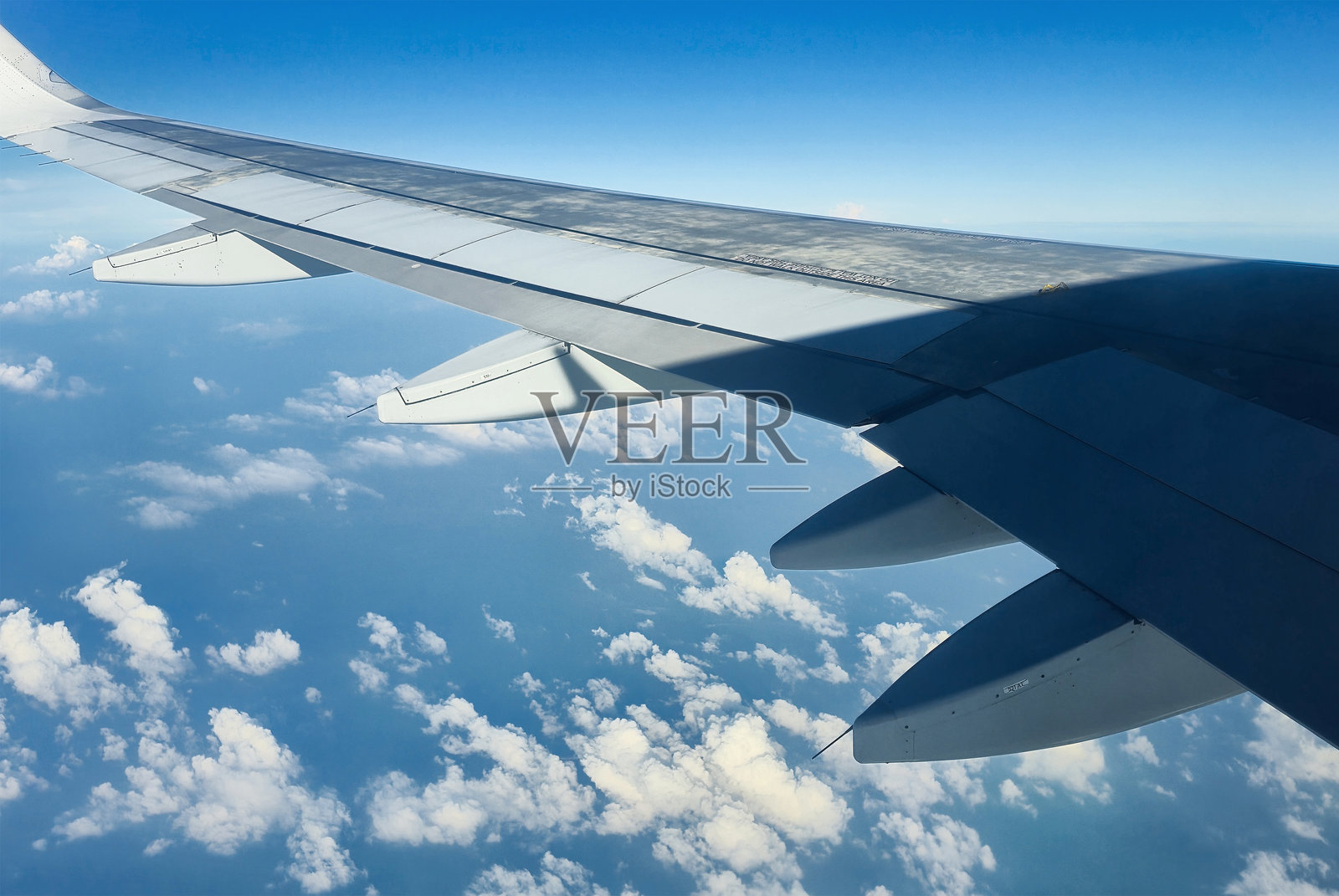 从飞机客舱看到的机翼，上方是印度尼西亚海群岛上阳光明媚的蓝天，点缀着朵朵白云。照片摄影图片