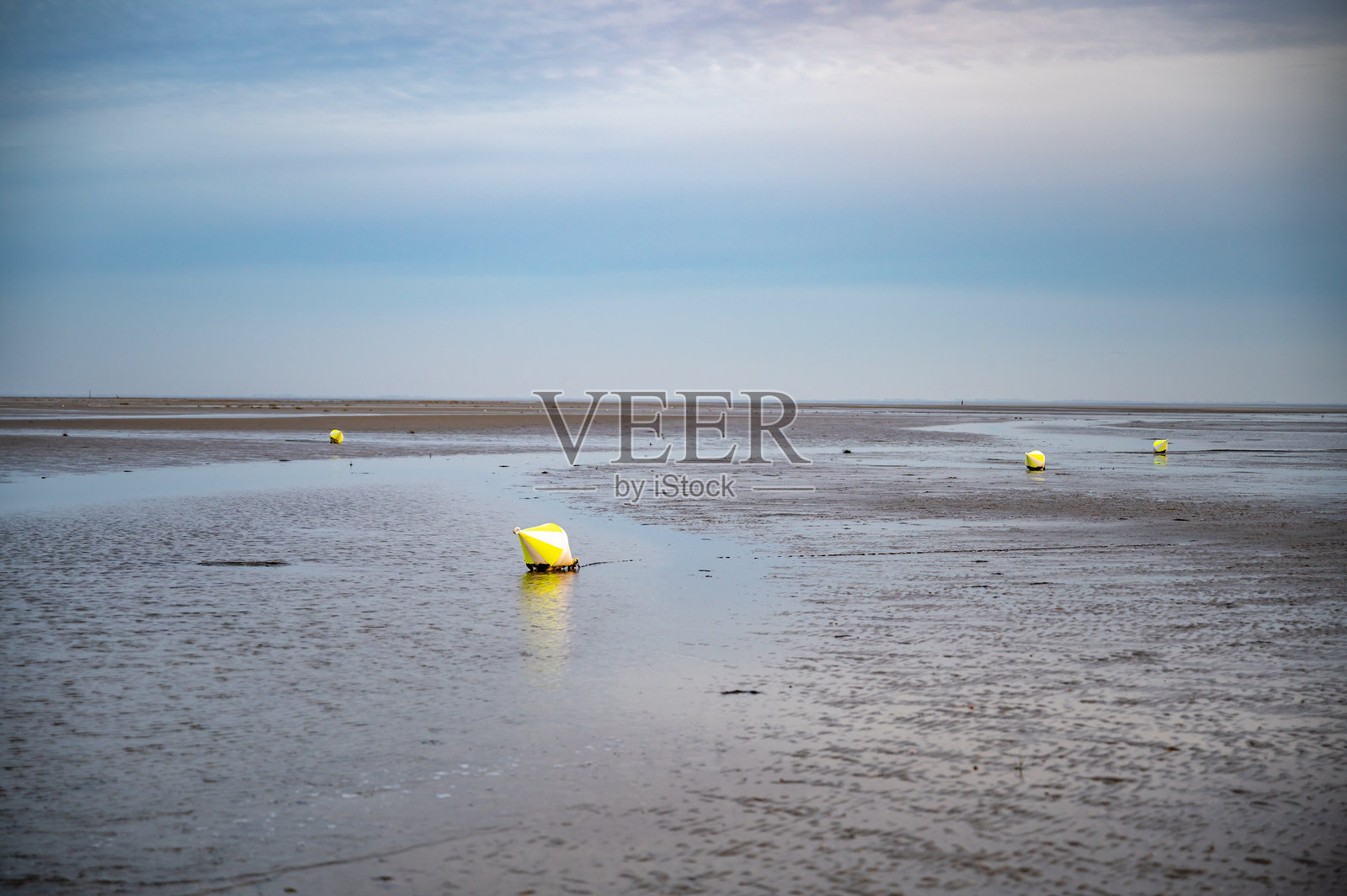 孤独的黄色浮标漂浮在广阔、平坦、潮湿的陆地上，天空多云，位于德国北海的圣彼得奥尔丁。照片摄影图片