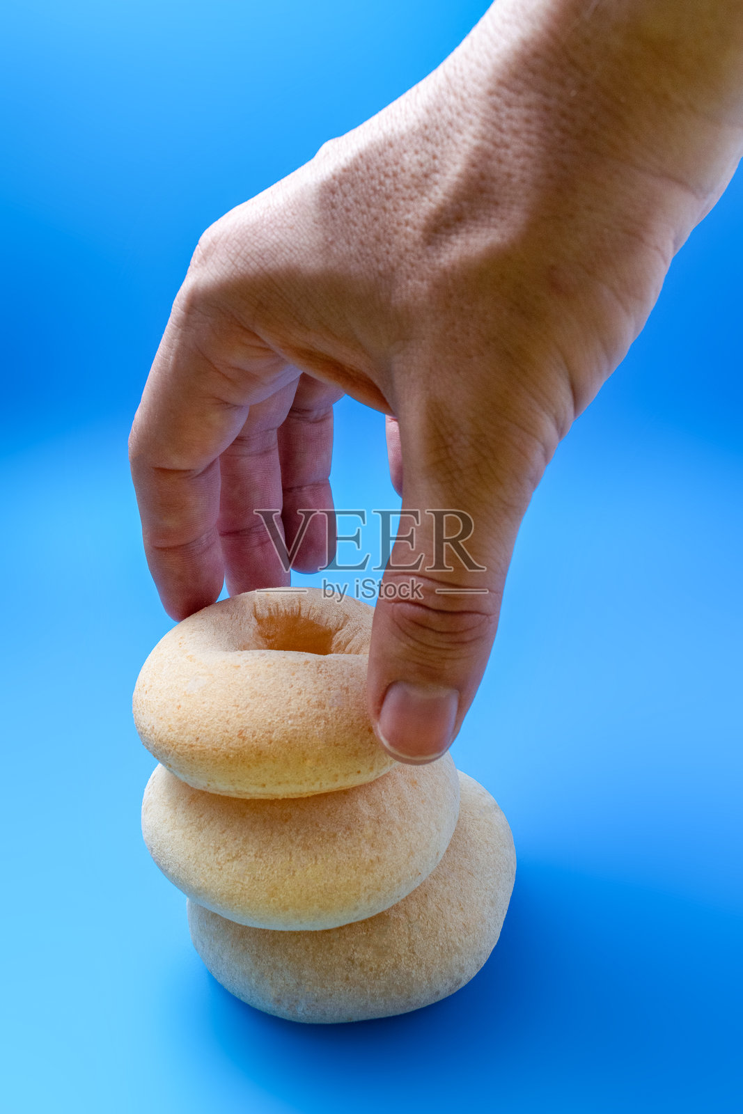 一只人手从一堆新鲜的木薯卷中拿起一个，背景是鲜艳的蓝色。照片摄影图片