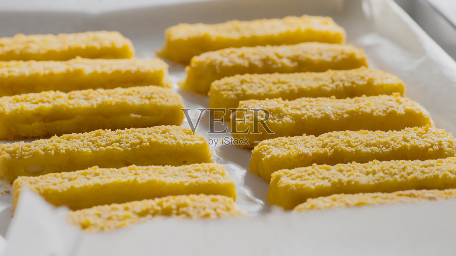 面包糠裹炸鱼条整齐地排列在烘焙纸上，准备就绪照片摄影图片