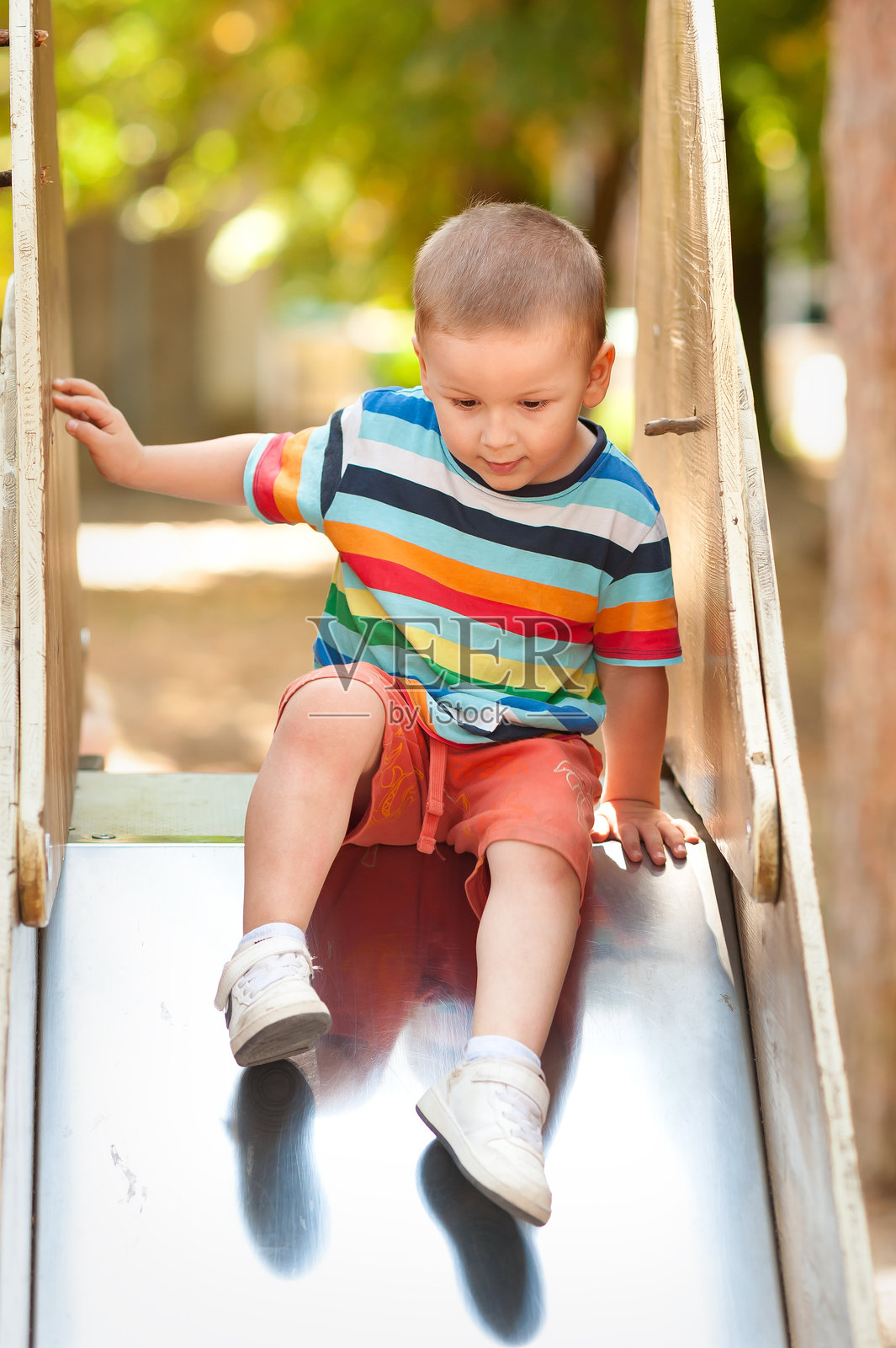 阳光明媚的户外游乐场里，一个小男孩正在滑滑梯照片摄影图片